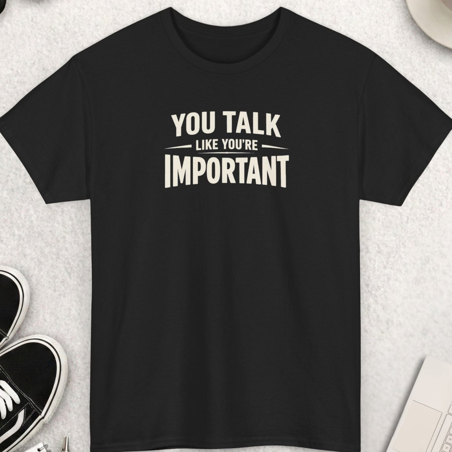 Black t-shirt with 'YOU TALK LIKE YOU'RE IMPORTANT' text on a light gray surface with shoes, coffee, and accessories.