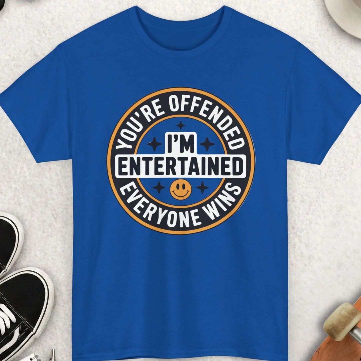Blue t-shirt with humorous graphic design on a light gray surface with accessories.