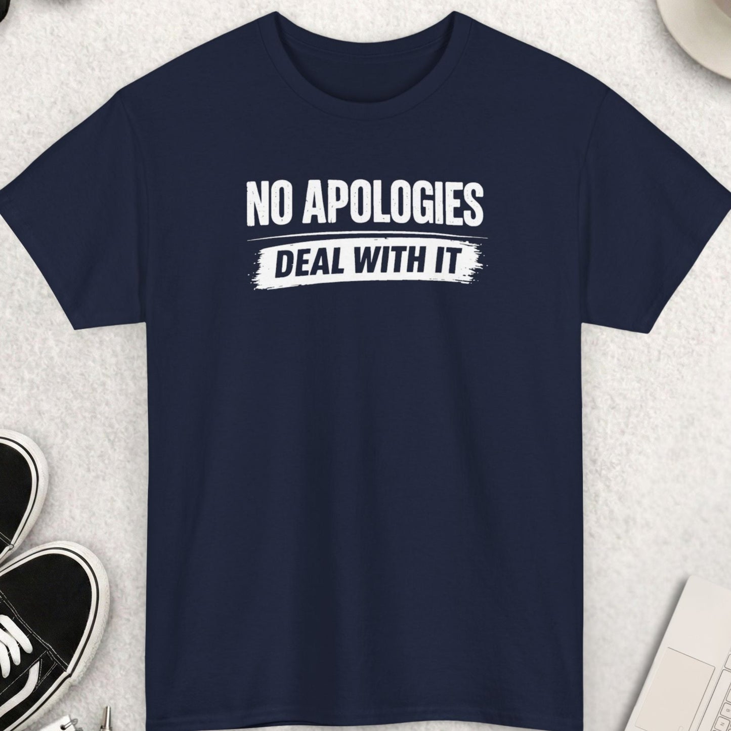 Navy blue t-shirt with 'No Apologies Deal With It' text on a light gray surface with accessories.