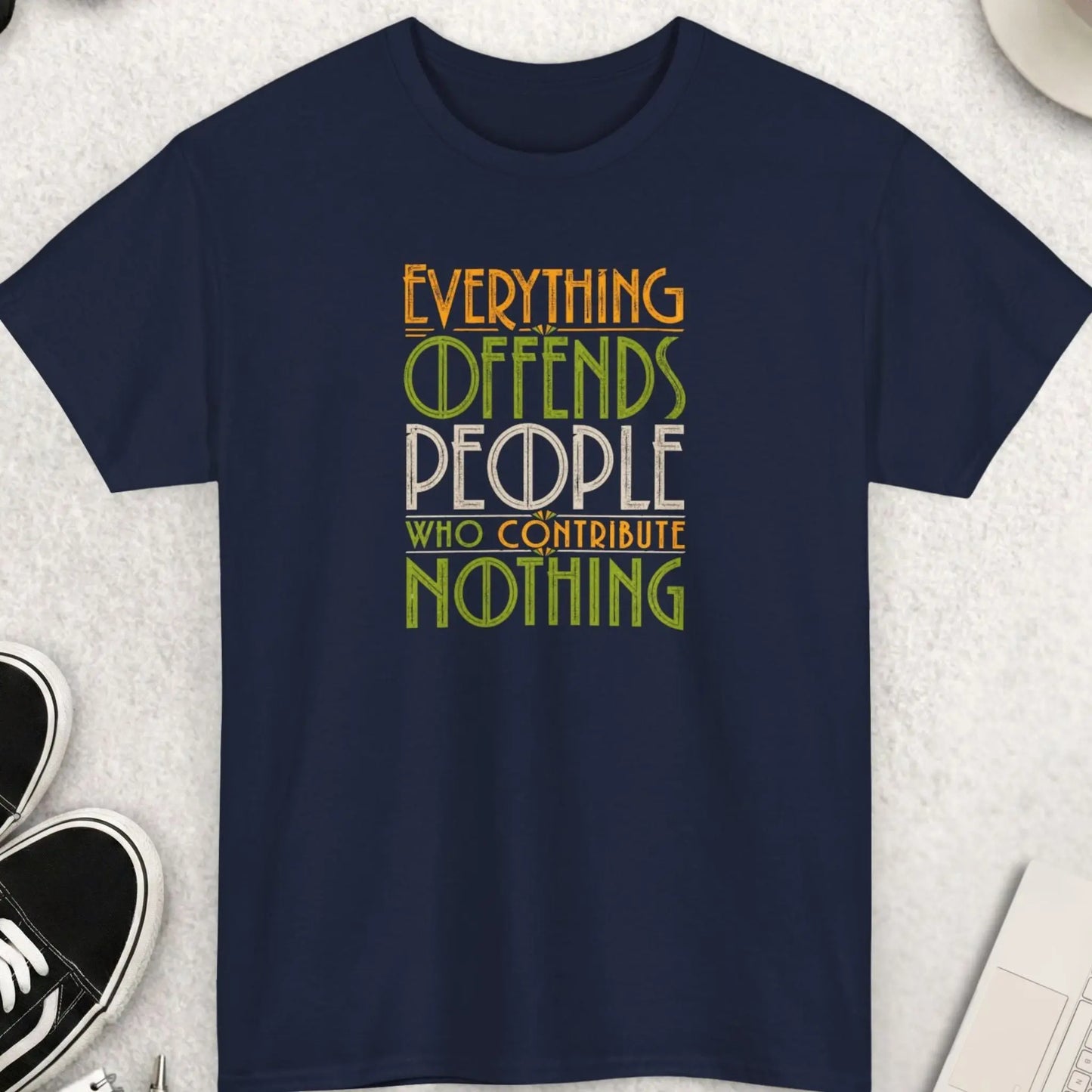 Navy blue sarcastic graphic tee featuring distressed retro typography reading “Everything Offends People Who Contribute Nothing” in green, cream, and gold vintage-style lettering.