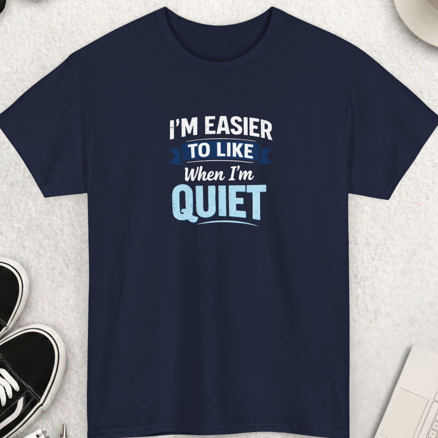 Navy blue t-shirt with humorous text on a light gray surface with accessories.