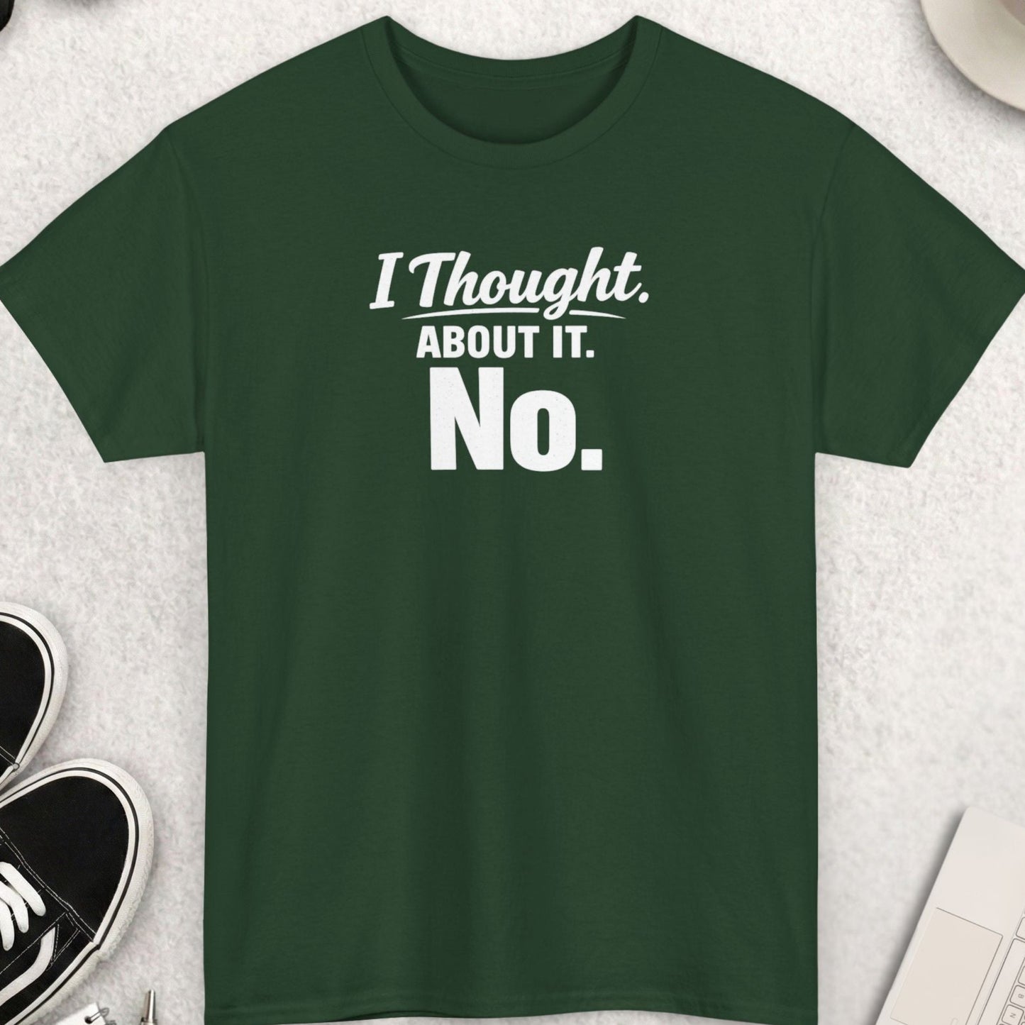Green t-shirt with 'I Thought About It. No.' text on a light gray surface with accessories.
