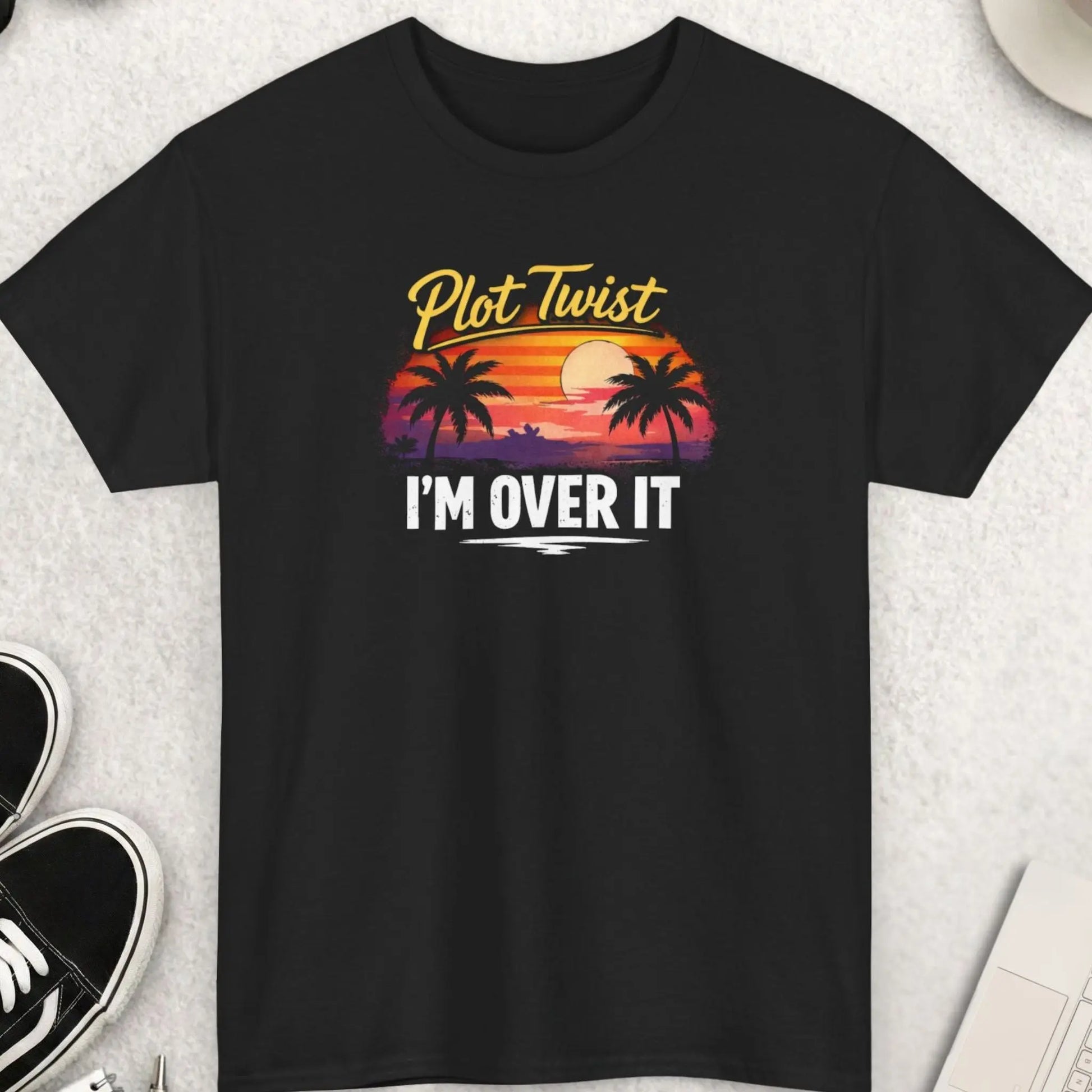 Black t-shirt with 'Plot Twist I'm Over It' design on a light gray surface with accessories.
