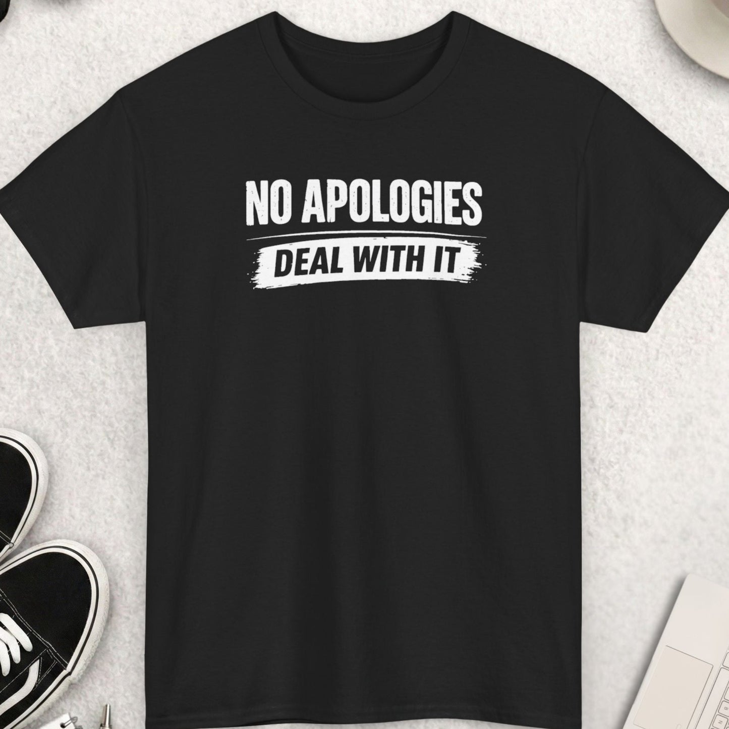 Black t-shirt with 'NO APOGIES DEAL WITH IT' text on a light gray surface with shoes, coffee, and accessories.