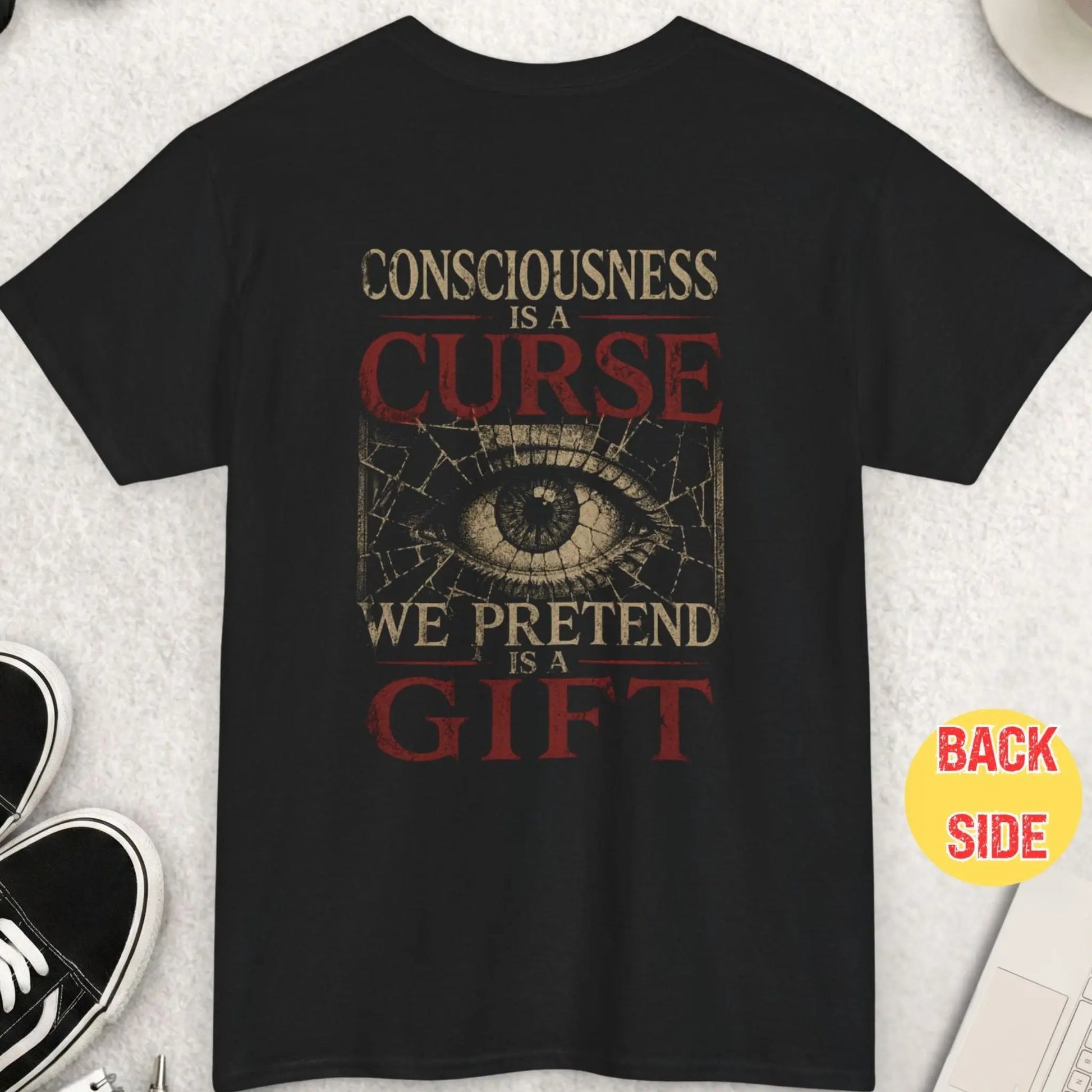 Black t-shirt featuring distressed typography reading “Consciousness is a curse we pretend it’s a gift” with cracked all-seeing eye graphic