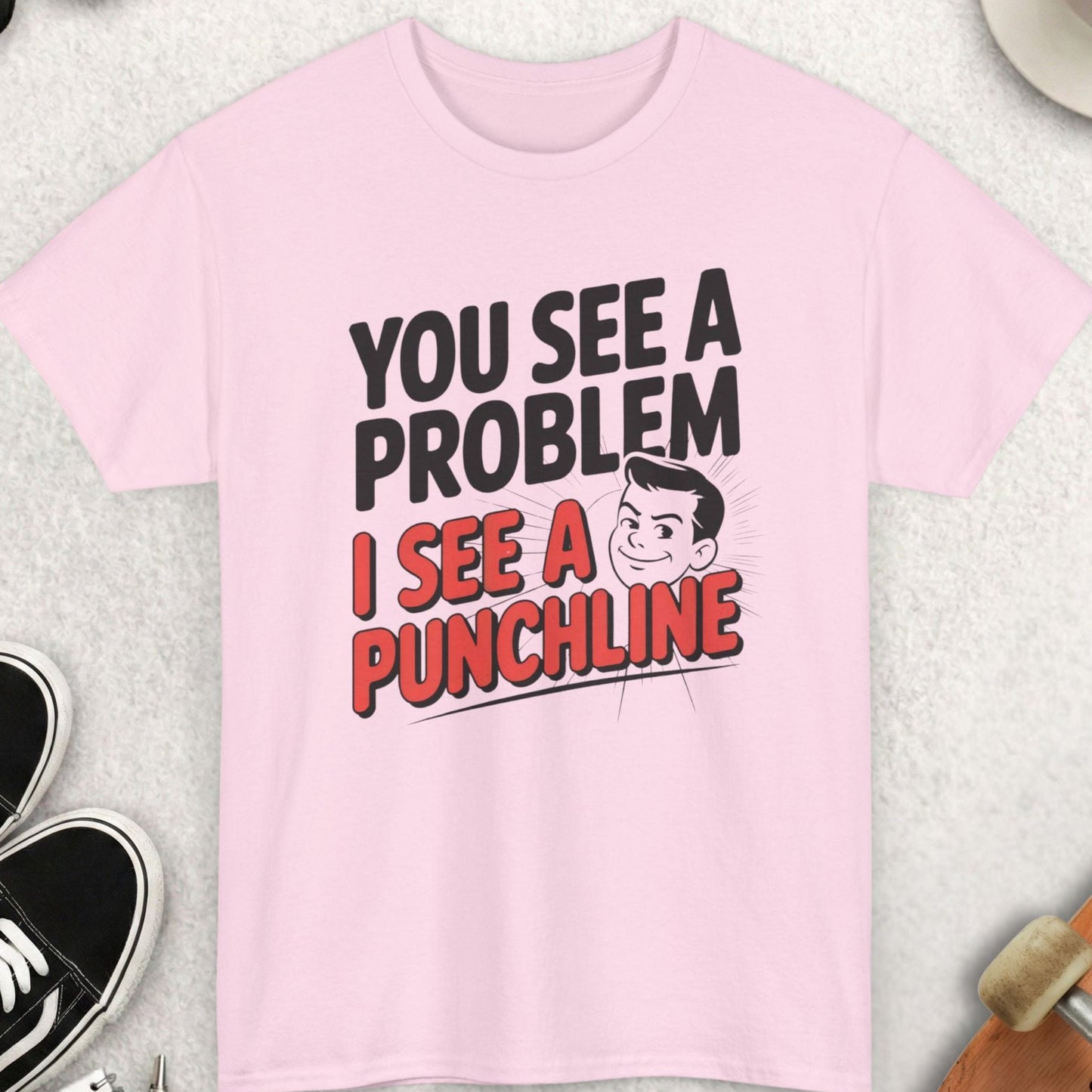 Pink t-shirt with humorous text design on a light gray surface with casual items around.