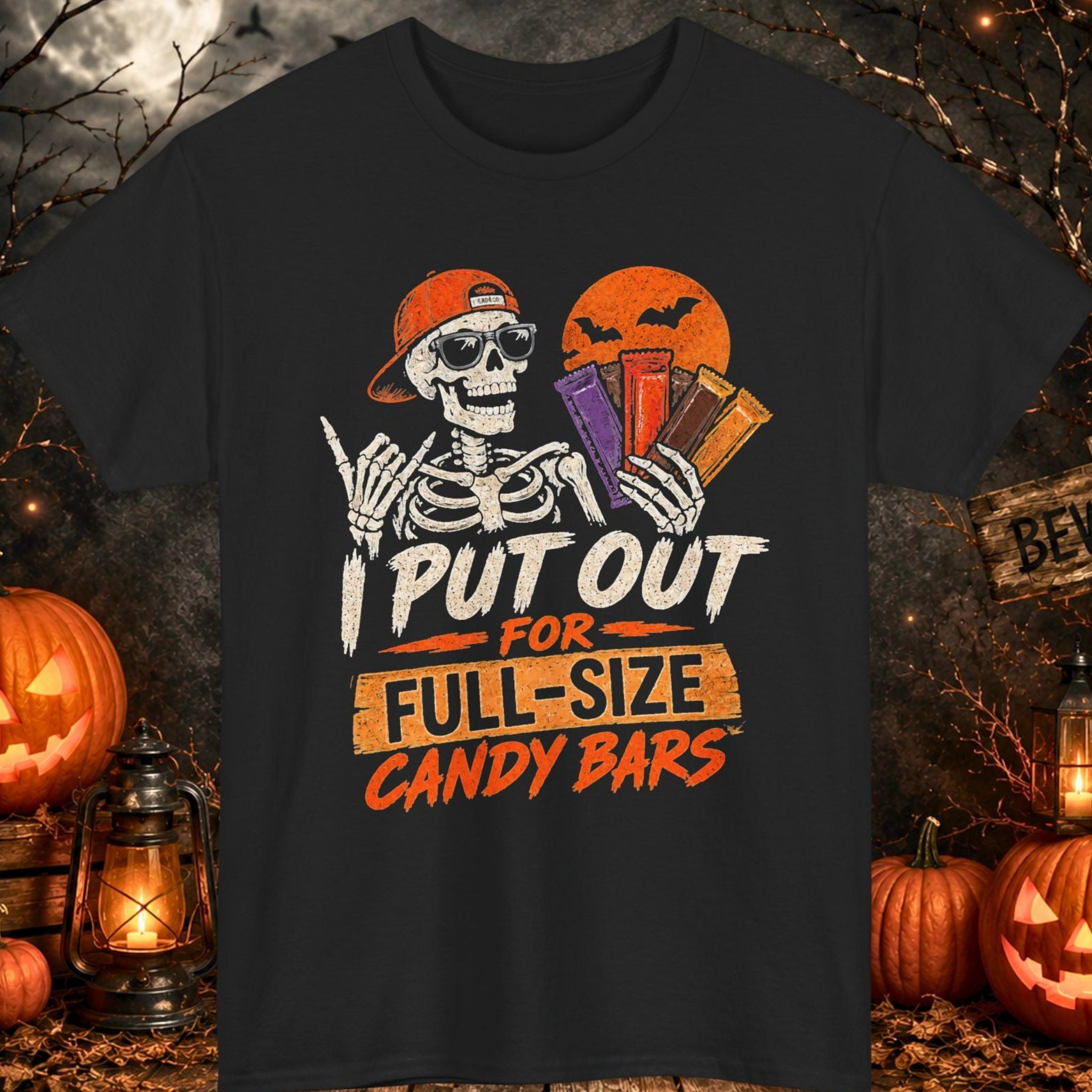 Mayhem Haus black Halloween T-shirt featuring a smiling skeleton wearing sunglasses and a backward cap while holding several oversized candy bars in front of an orange moon with bats. The distressed graphic includes the phrase, "I Put Out for Full-Size Candy Bars."