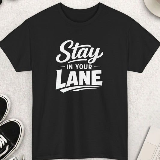 Black t-shirt with 'Stay in Your Lane' text on a light gray surface with shoes, coffee, and sunglasses.