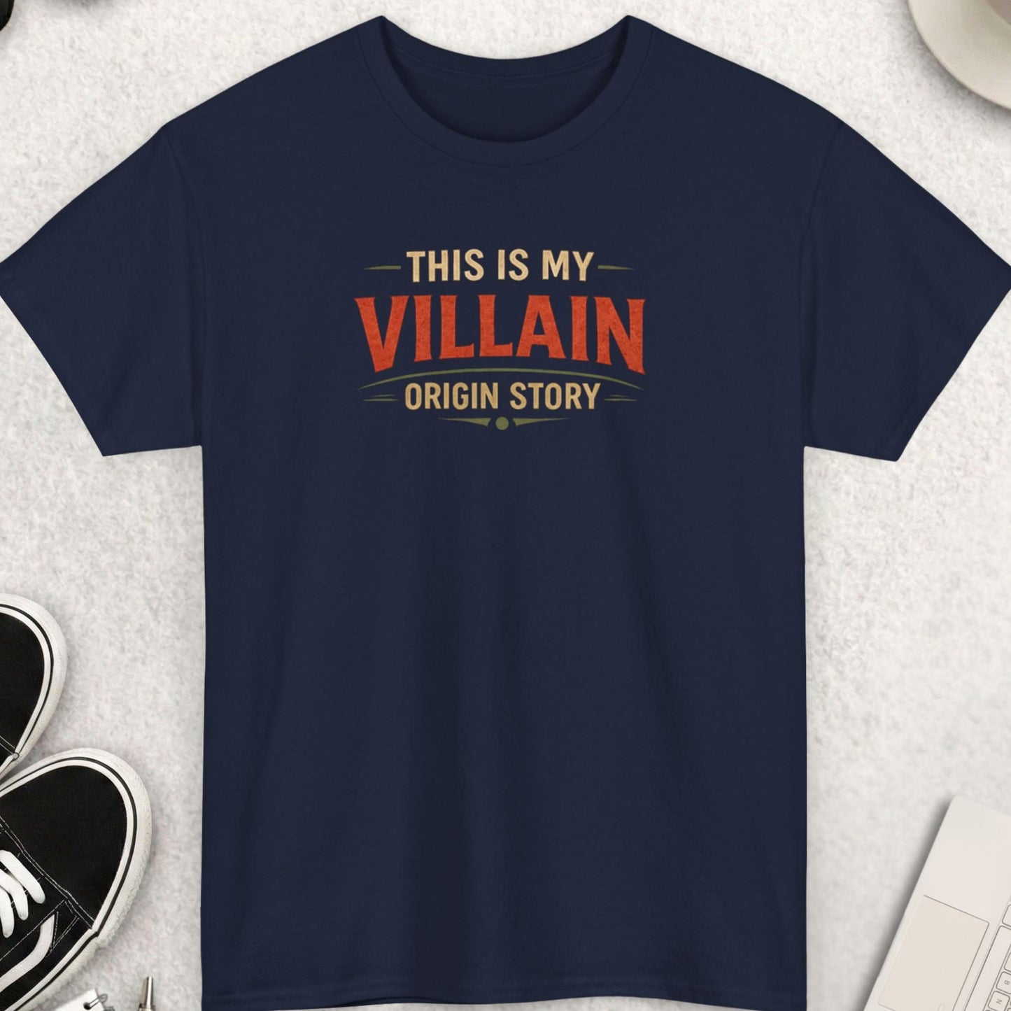 Navy blue t-shirt with 'This is my Villain Origin Story' text on a light gray surface with shoes, coffee, and accessories.