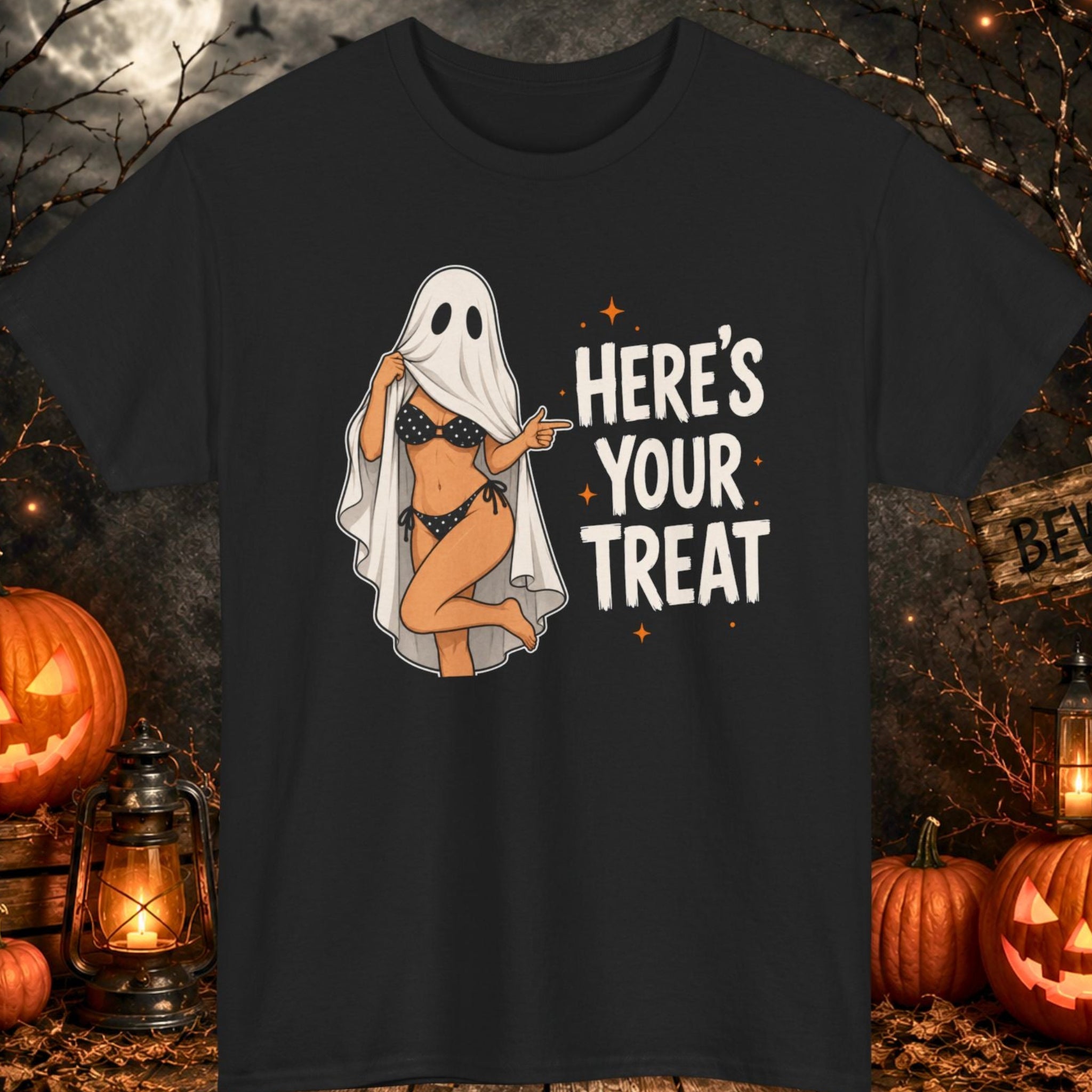 Mayhem Haus Halloween graphic t-shirt on a black shirt featuring a playful ghost costume lifting the front of the sheet to reveal a black polka-dot bikini. Bold white typography reads "HERE'S YOUR TREAT" with small orange star accents in a fun Halloween design.
