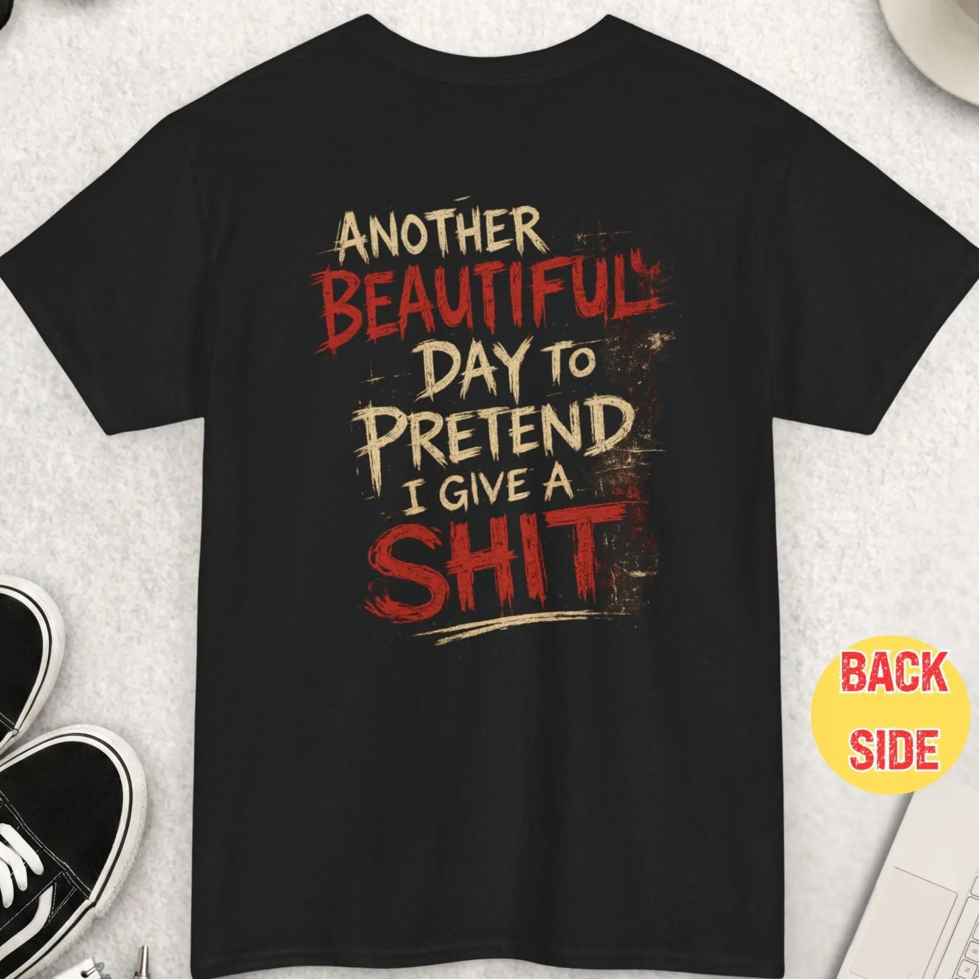 Black distressed graphic t-shirt featuring the phrase “Another Beautiful Day To Pretend I Give A Shit” in rough cream and red grunge typography with a dark humor streetwear aesthetic by Mayhem Haus.