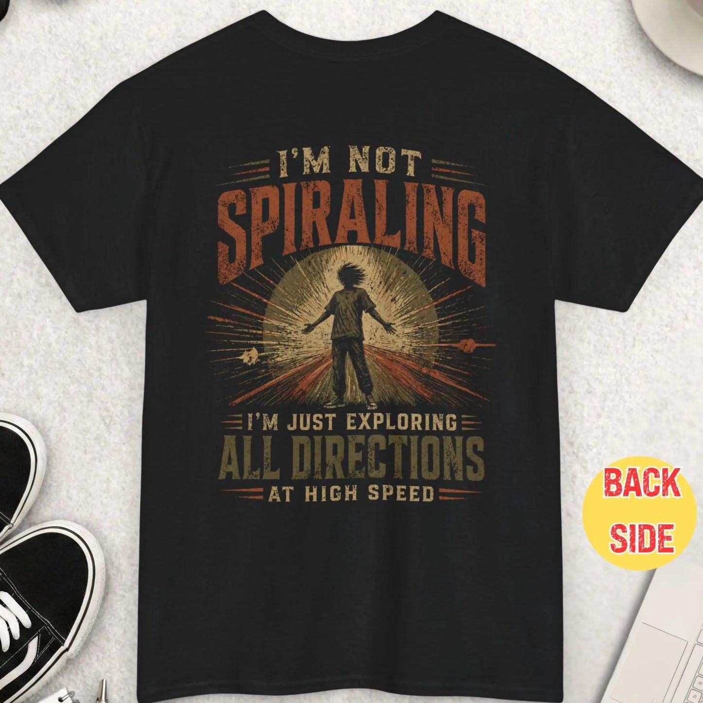 Black t-shirt with distressed typography reading “I’m not spiraling I’m just exploring all directions at high speed” with dynamic chaotic figure graphic