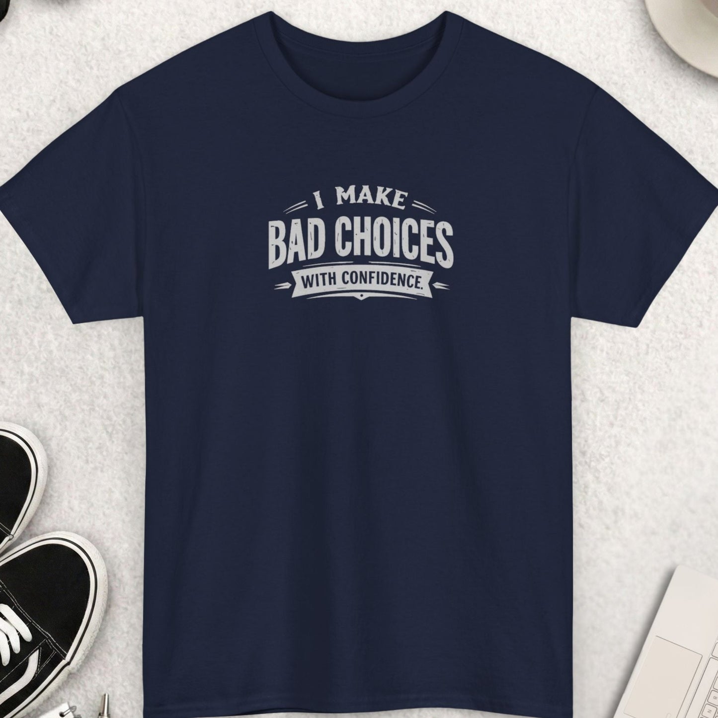Navy blue t-shirt with humorous text on a light gray surface with accessories.