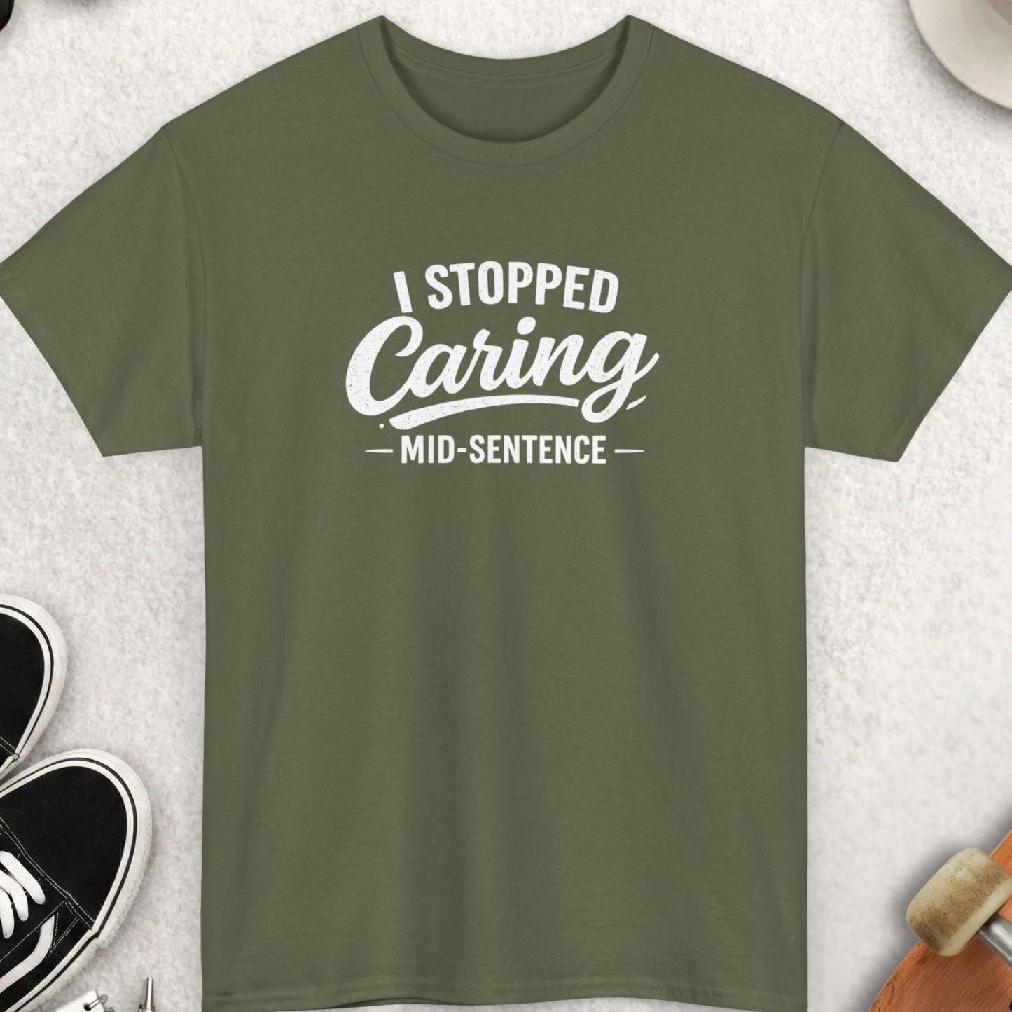 Green t-shirt with 'I Stopped Caring Mid-Sentence' text on a light gray surface with accessories.