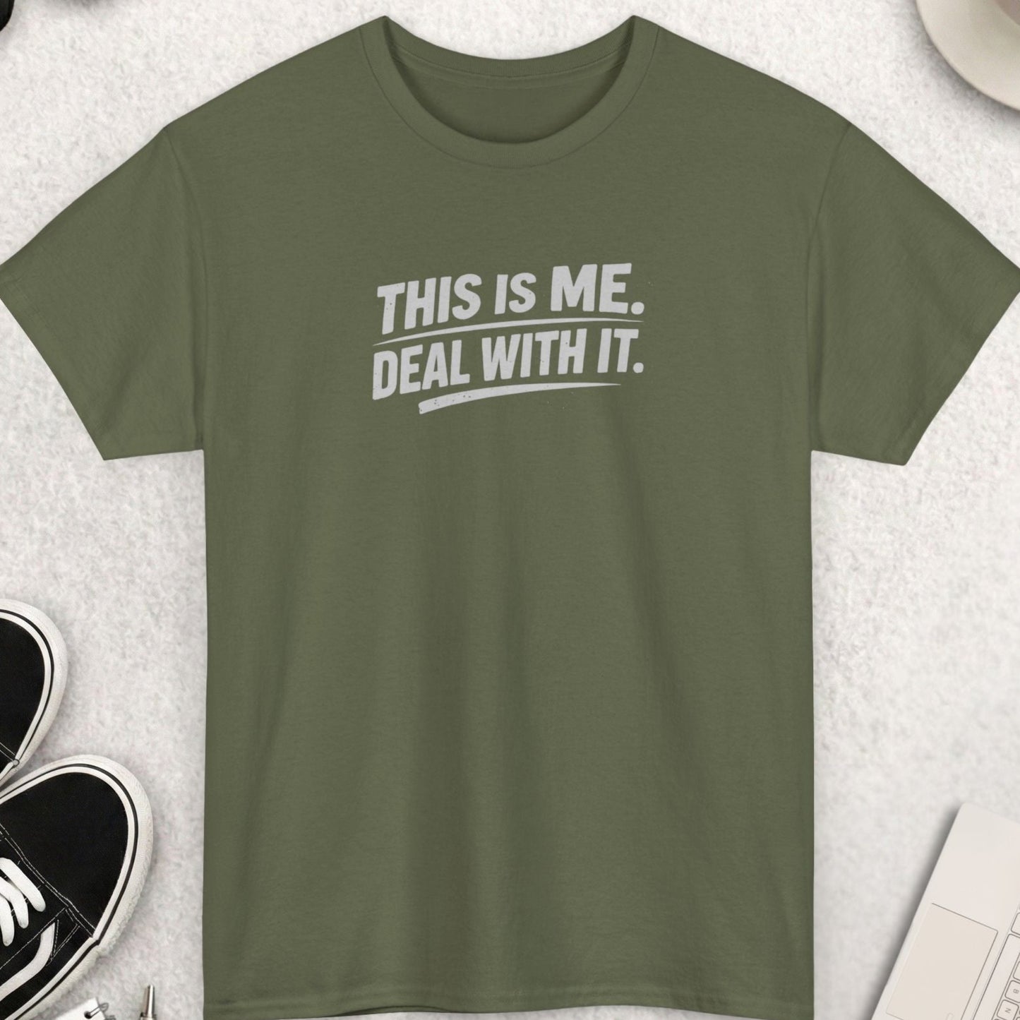 Green t-shirt with 'THIS IS ME. DEAL WITH IT.' text on a light gray surface with accessories.