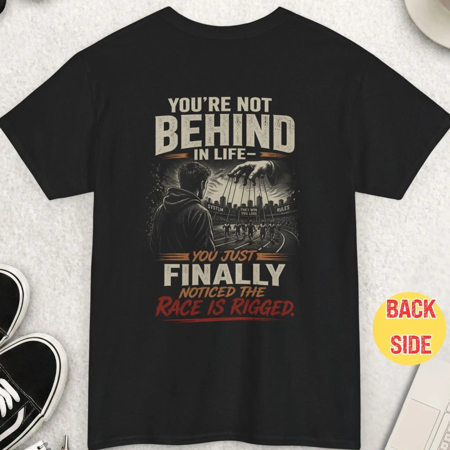 Black t-shirt with bold “race is rigged” message featuring man observing controlled runners with puppet strings and dystopian system illustration