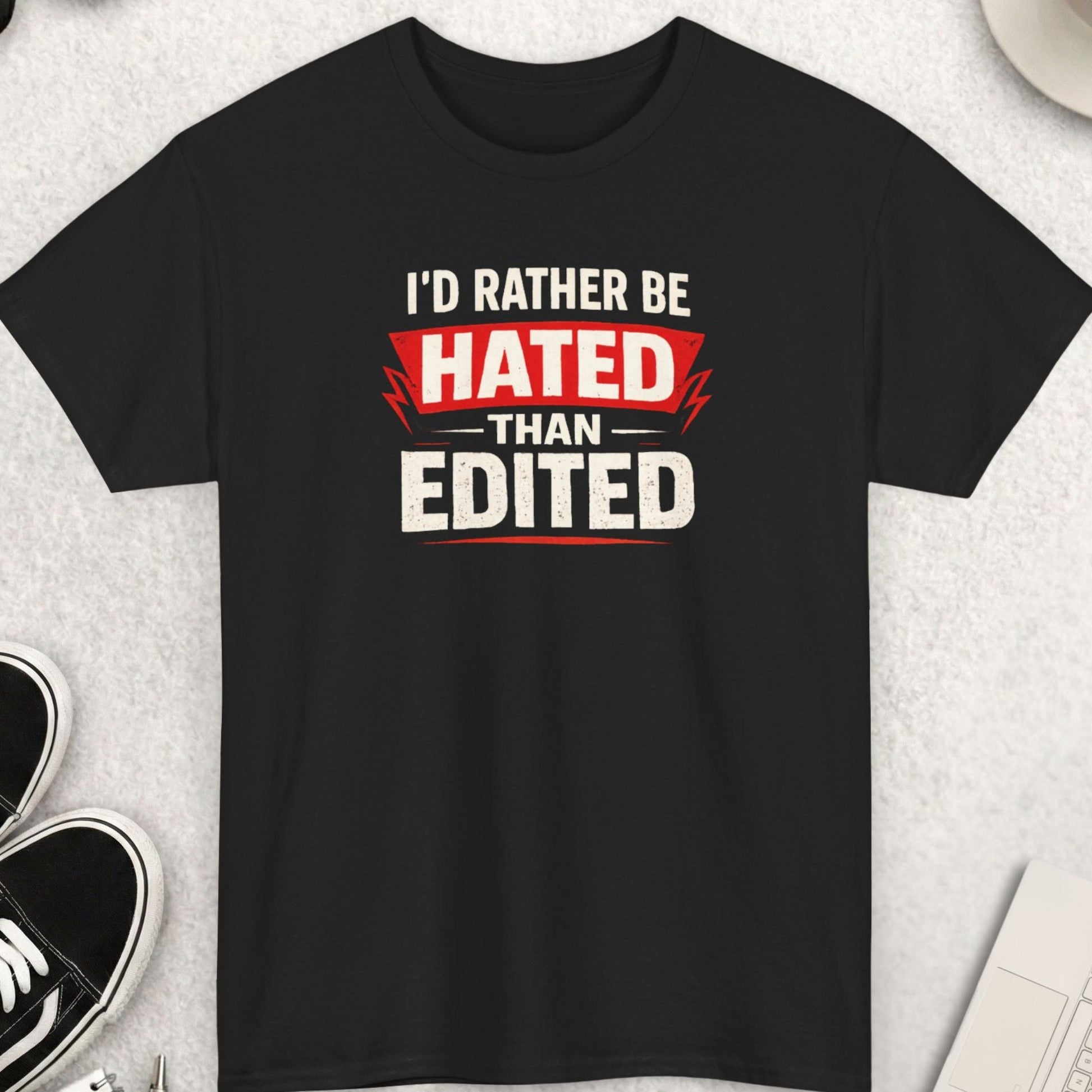 Black t-shirt with 'I'd Rather Be Hated Than Edited' text on a light gray surface with shoes, coffee, and accessories.