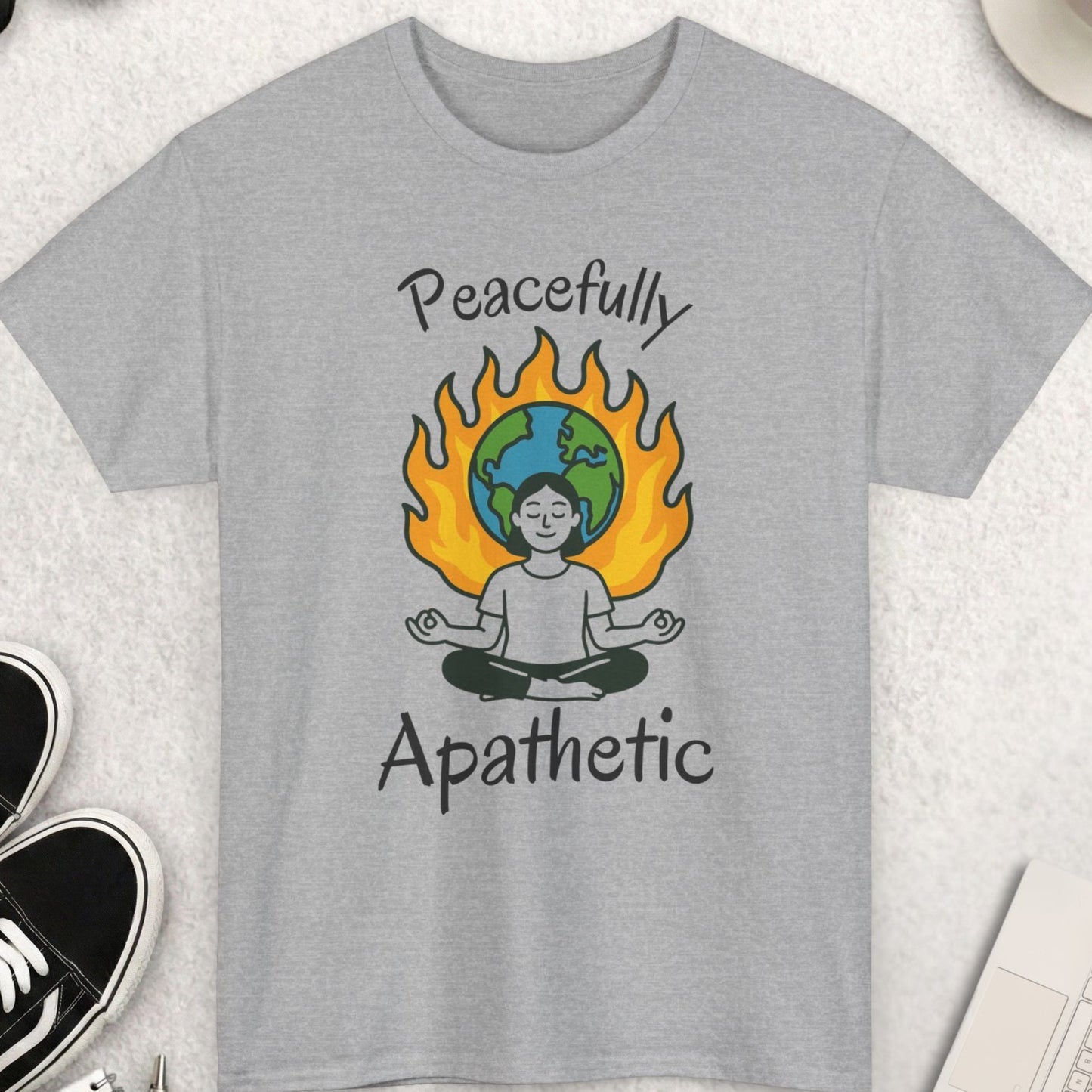Gray t-shirt with 'Peacefully Apathetic' design on a light surface with accessories.