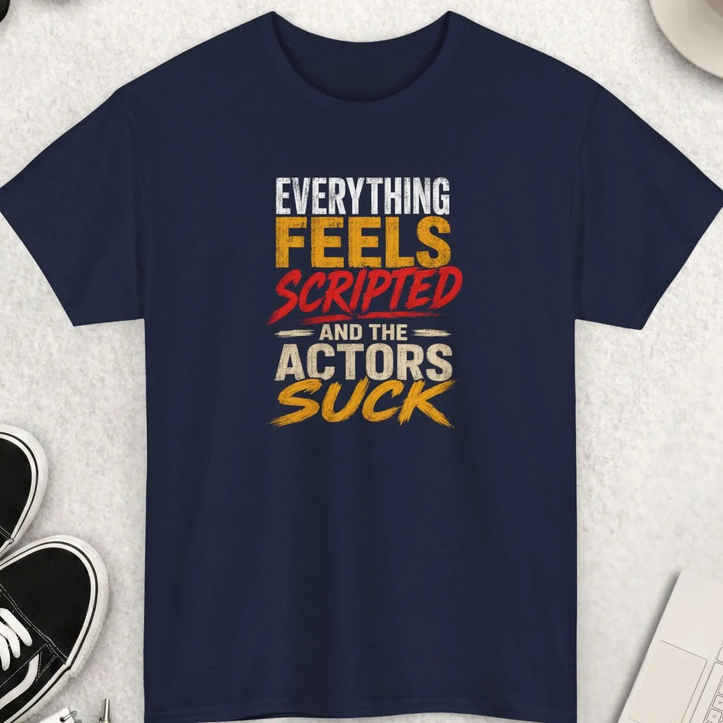 Navy blue sarcastic graphic tee featuring distressed white, red, and gold lettering reading “Everything Feels Scripted And The Actors Suck” in a bold grunge-style typography design.