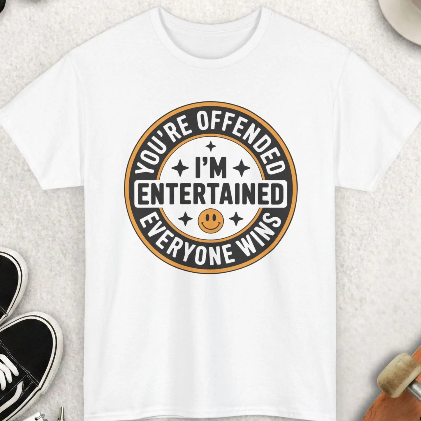 White t-shirt with a humorous graphic design on a light surface with casual items around.