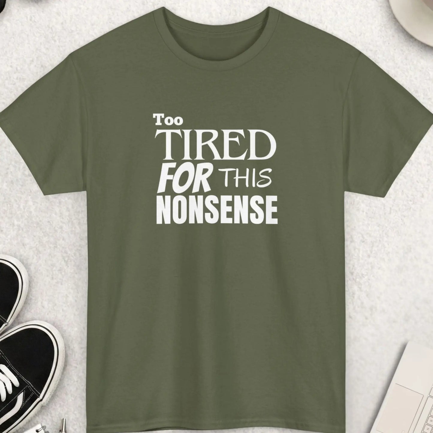 Green t-shirt with 'Too Tired for This Nonsense' text on a light gray surface with accessories.