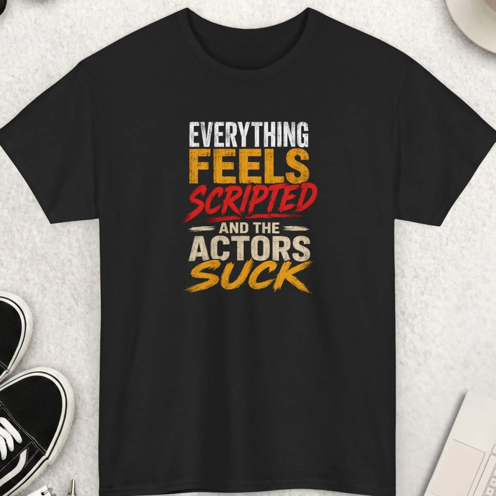 Black distressed graphic t-shirt featuring the phrase “Everything Feels Scripted And The Actors Suck” in oversized white, red, and gold typography with a grunge-inspired streetwear aesthetic.