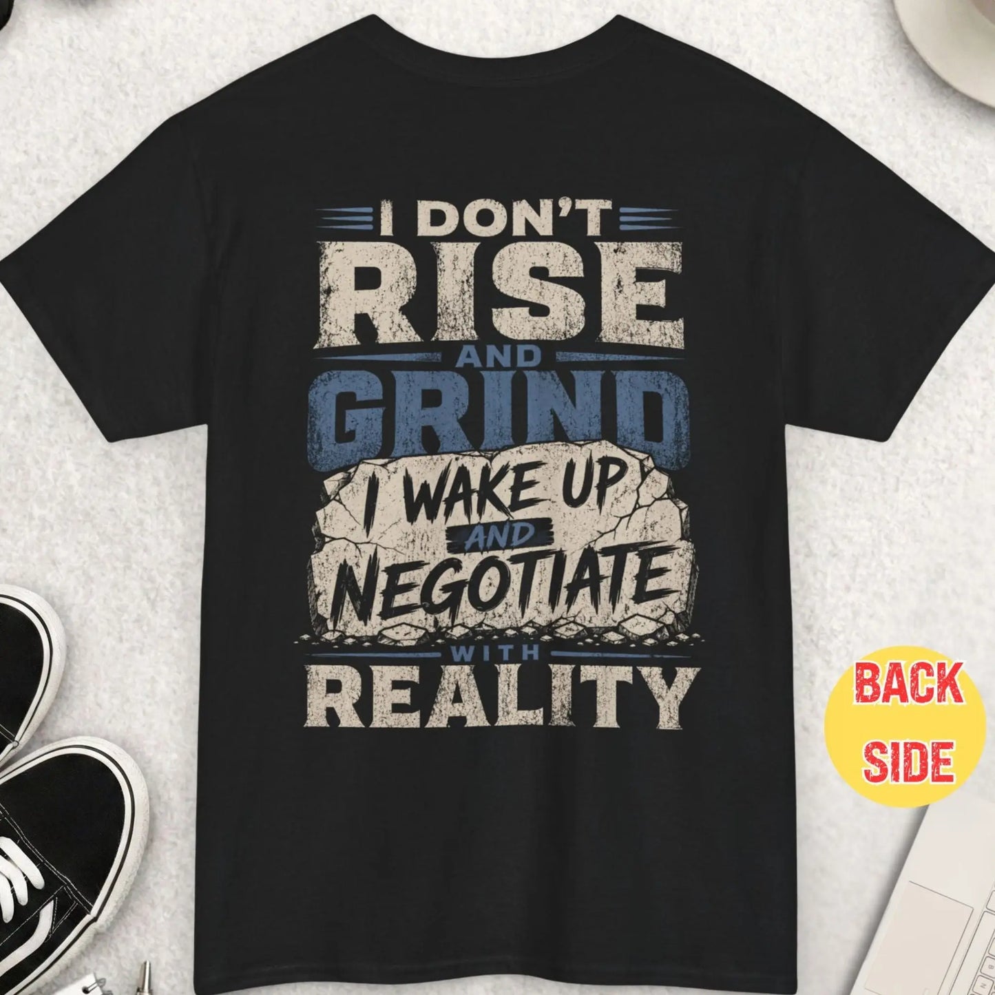 Black t-shirt with distressed typography reading “I don’t rise and grind I wake up and negotiate with reality” with cracked stone style graphic