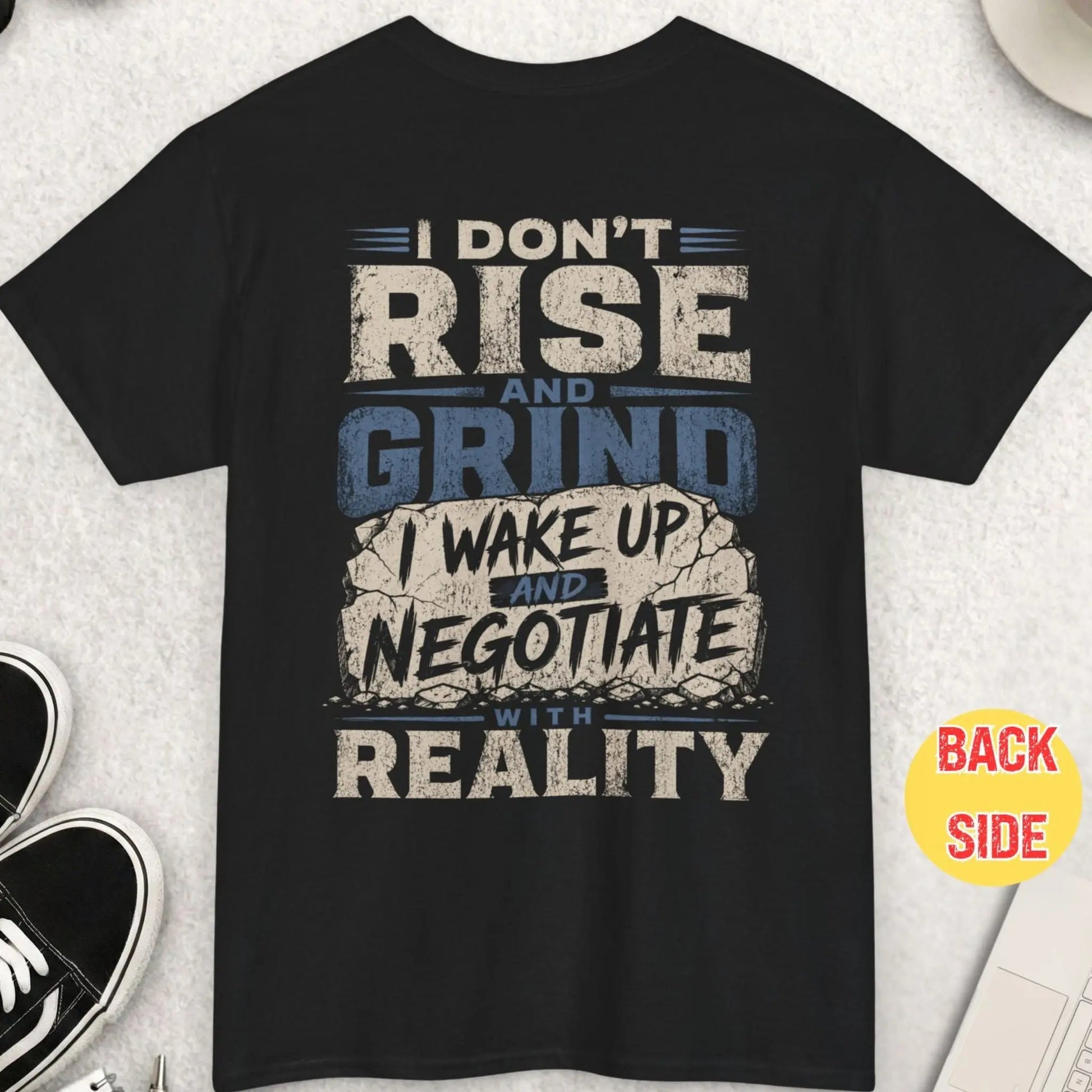 Black t-shirt with distressed typography reading “I don’t rise and grind I wake up and negotiate with reality” with cracked stone style graphic