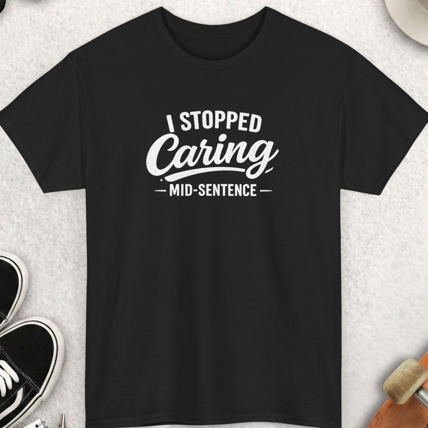 Black t-shirt with 'I Stopped Caring Mid-Sentence' text on a light gray surface with accessories.