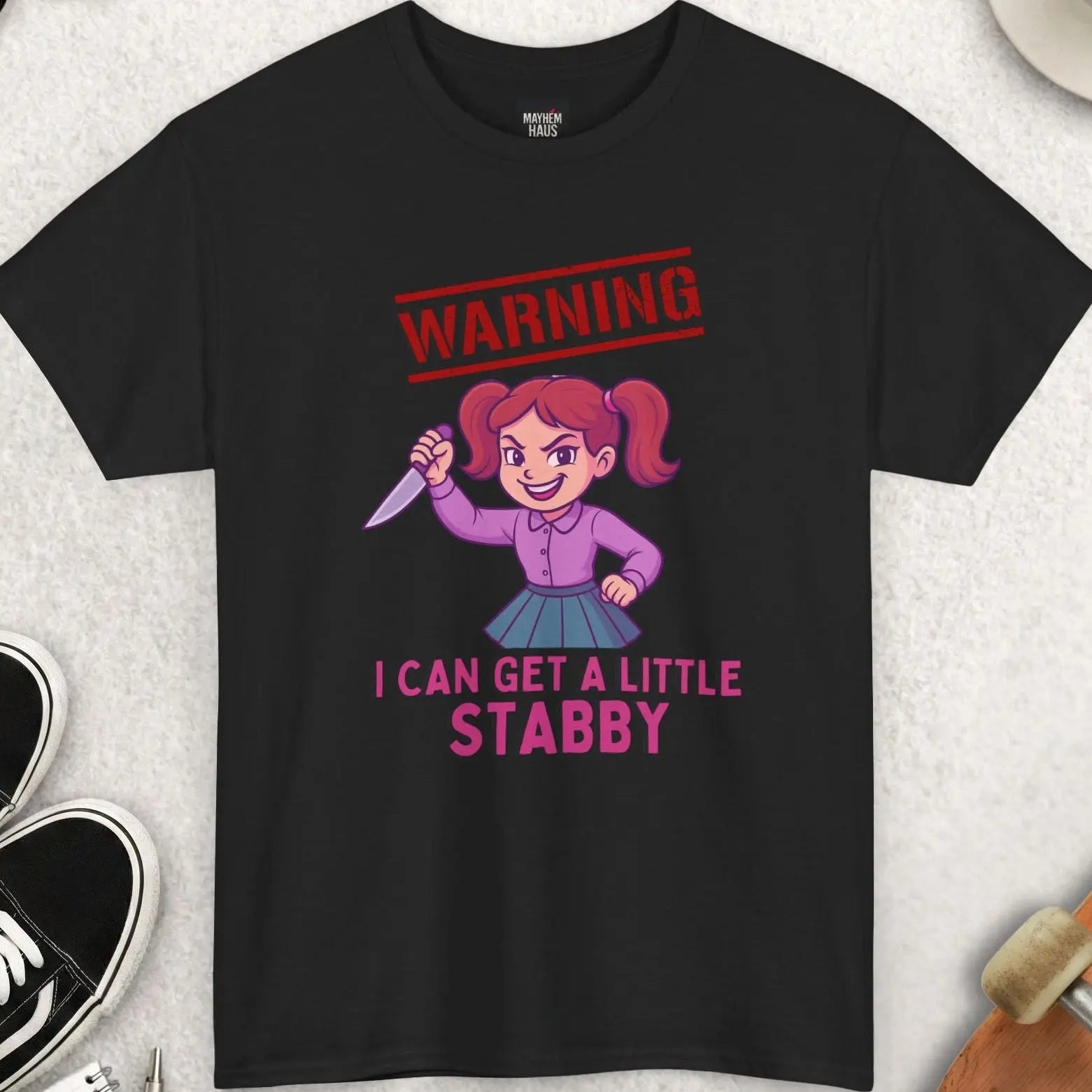 Black t-shirt with graphic design and text on a light gray surface with accessories.