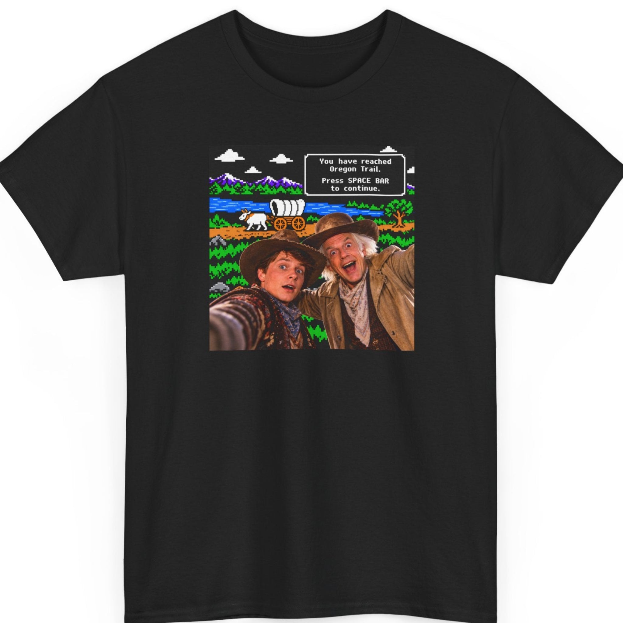 Mayhem Haus Oregon Trail parody black t-shirt featuring two excited time-traveling cowboys taking a selfie in front of a colorful pixelated wagon trail, with retro video game text reading “You have reached Oregon Trail. Press SPACE BAR to continue.”