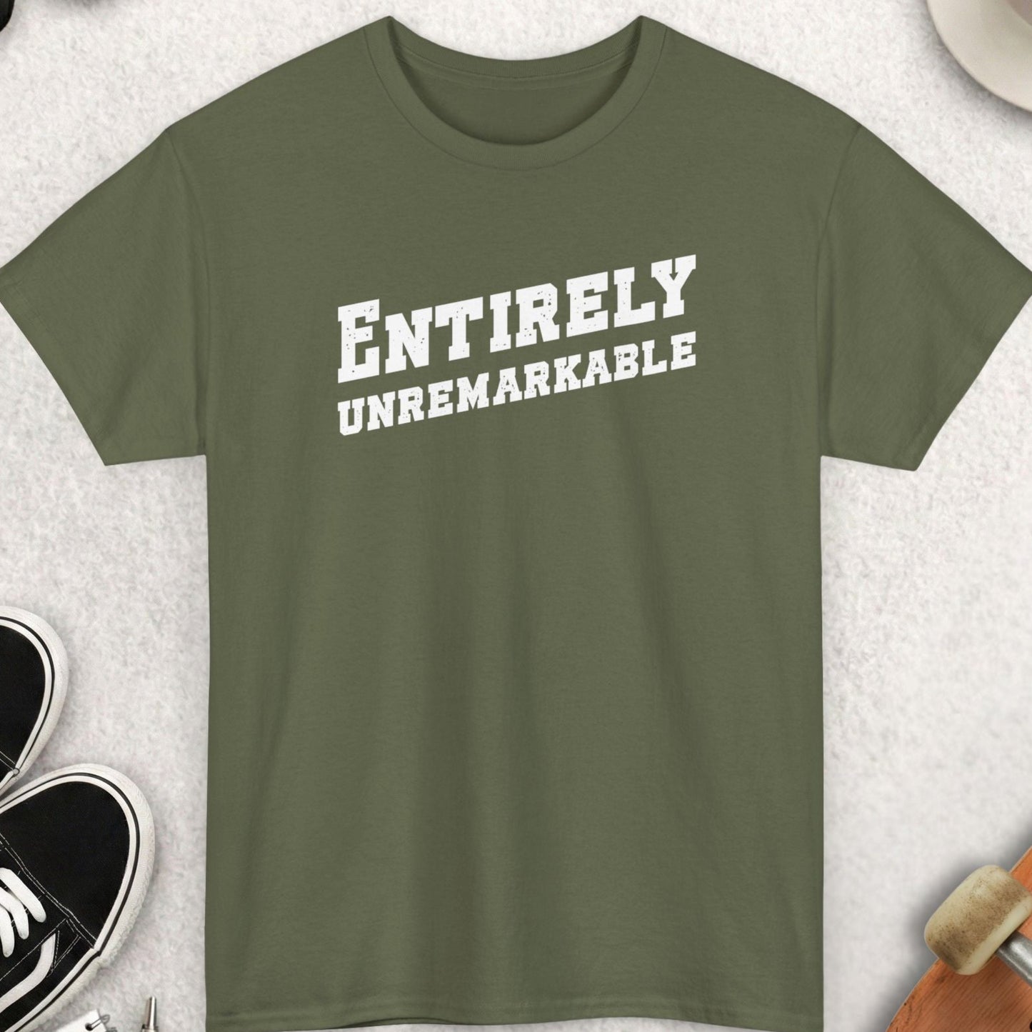 Green t-shirt with 'ENTIRELY UNREMARKABLE' text, surrounded by casual items on a light surface.