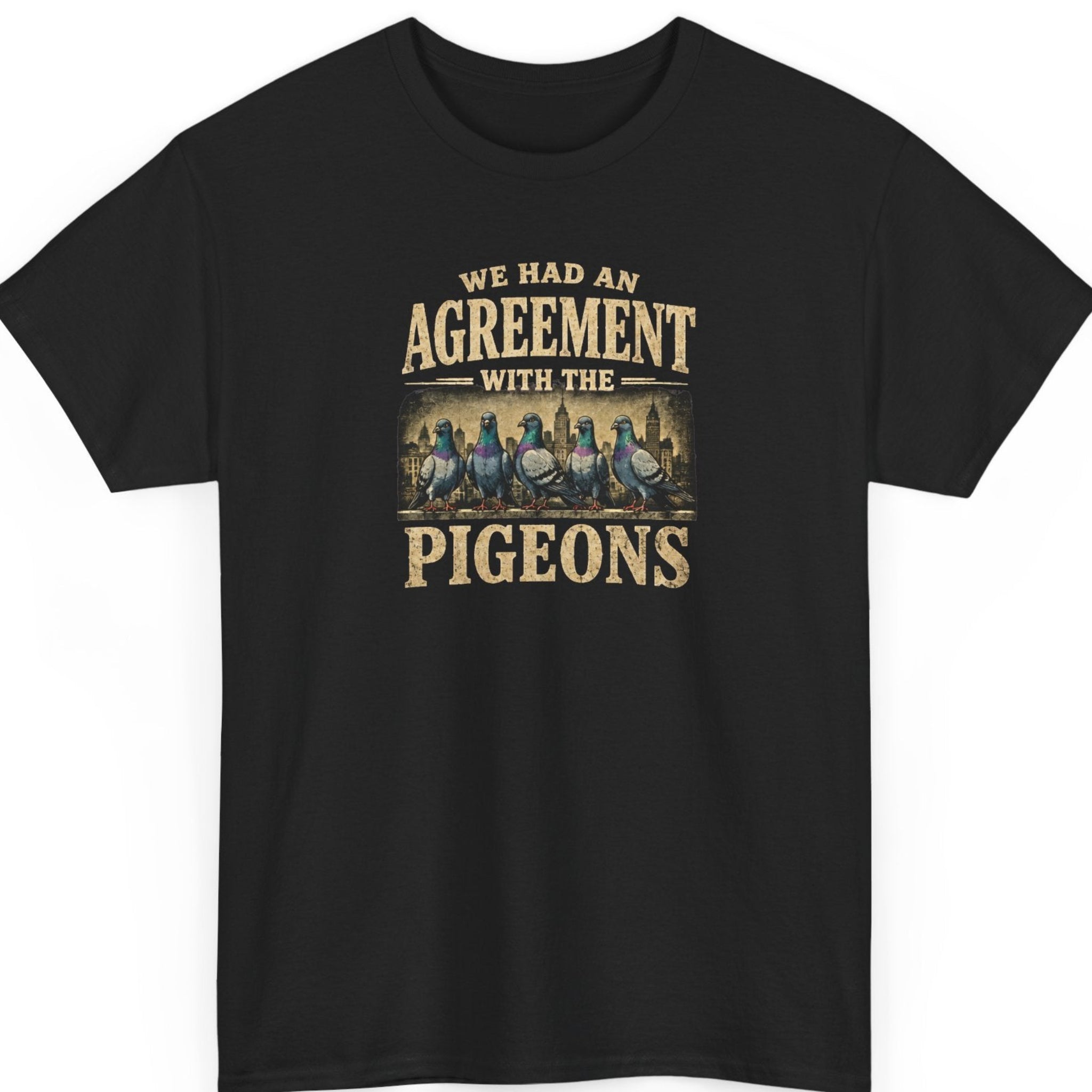 Mayhem Haus deadpan surrealism t-shirt on a black shirt featuring a distressed vintage typography design that reads, “We Had an Agreement With the Pigeons,” with five suspicious-looking pigeons standing in front of an urban skyline.