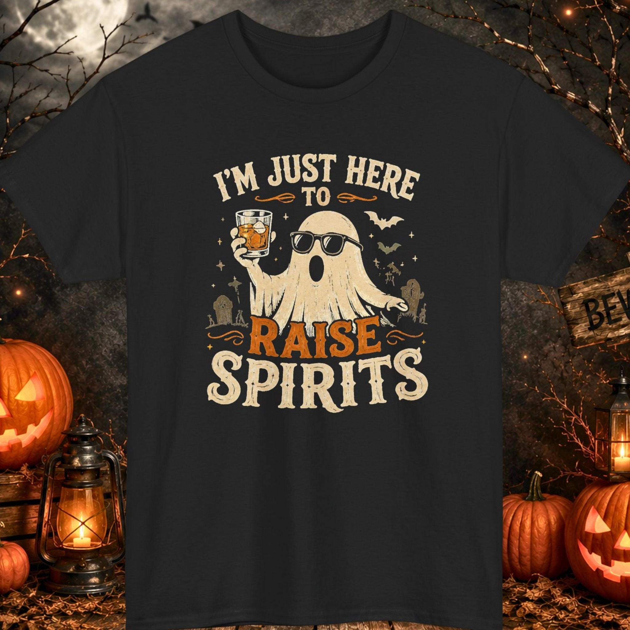Mayhem Haus black Halloween T-shirt featuring a ghost wearing sunglasses while raising a cocktail beneath the phrase "I'm Just Here to Raise Spirits." The distressed vintage-style design includes bats, a graveyard backdrop, and retro Halloween artwork, creating the perfect graphic tee for Halloween parties, breweries, and spooky season celebrations.