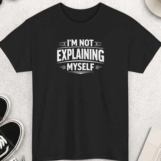 Black t-shirt with 'I'm not explaining myself' text on a light gray surface with shoes, coffee, and accessories.
