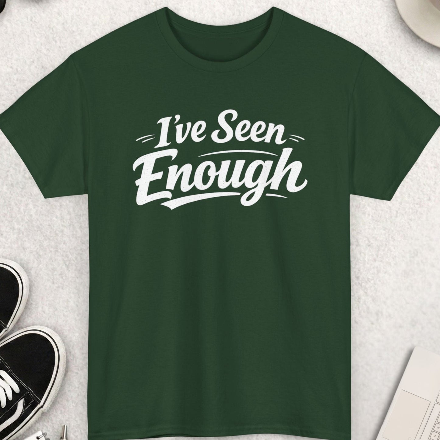 Green t-shirt with 'I've Seen Enough' text on a light gray surface with shoes, sunglasses, and a cup.