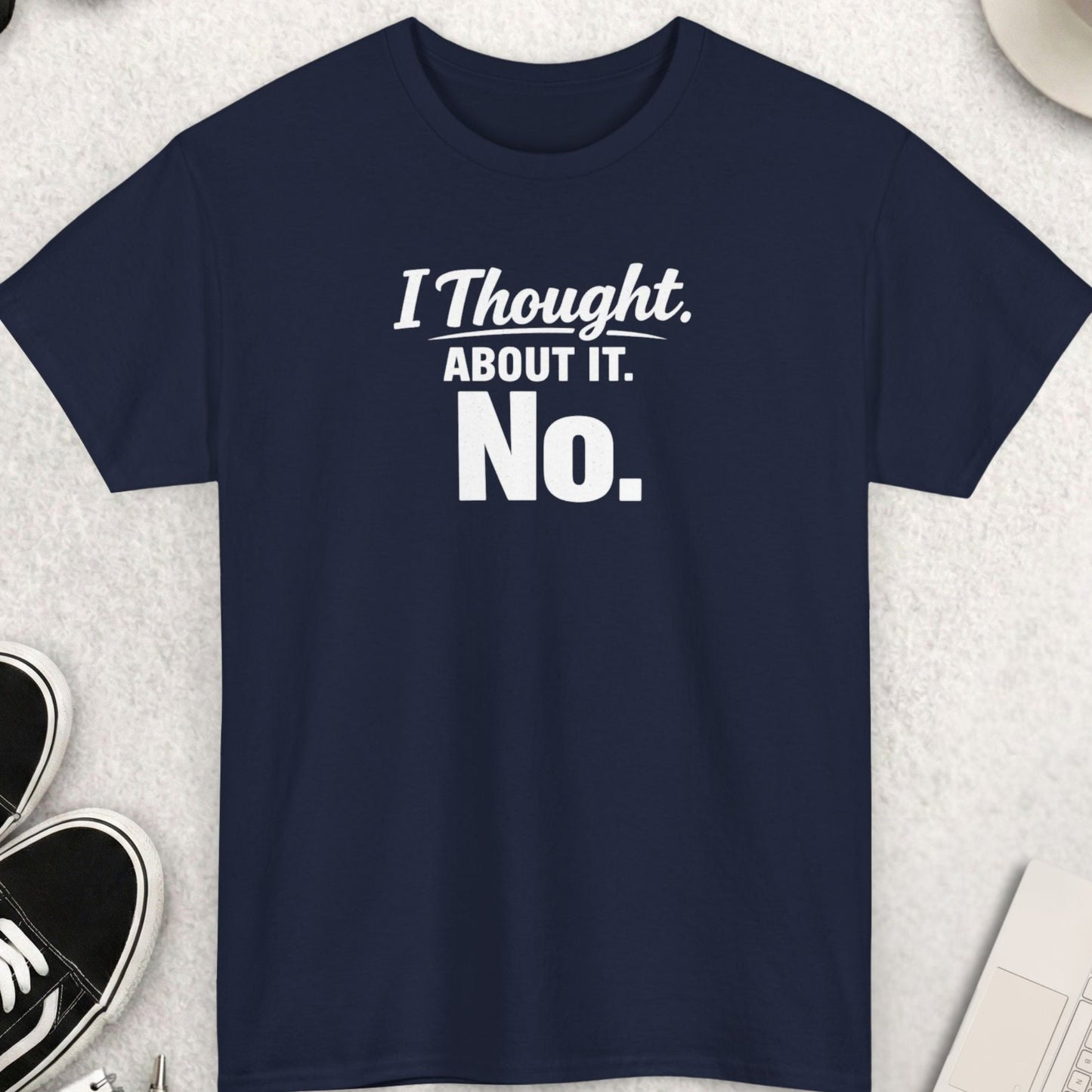 Navy blue t-shirt with 'I Thought About It. No.' text on a light gray surface with accessories.