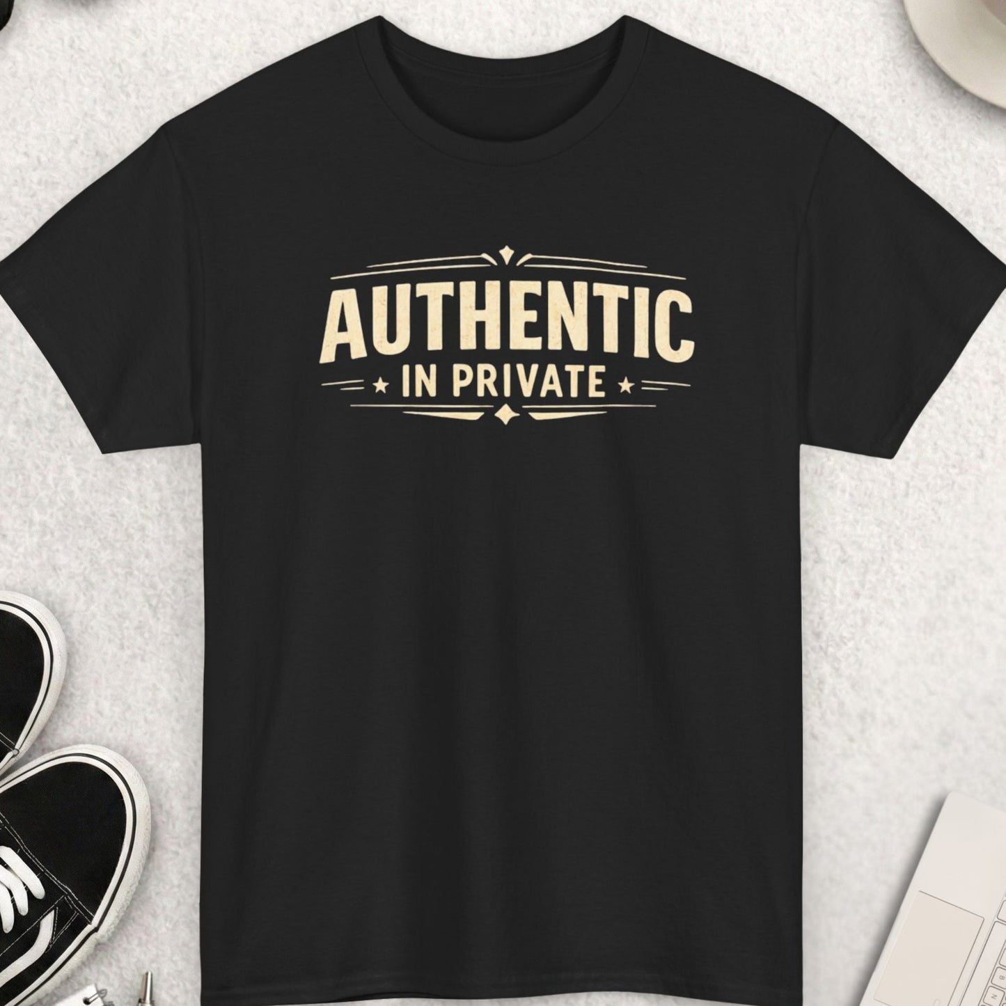 Black t-shirt with 'Authentic in Private' text on a light gray surface with shoes, coffee, and accessories.