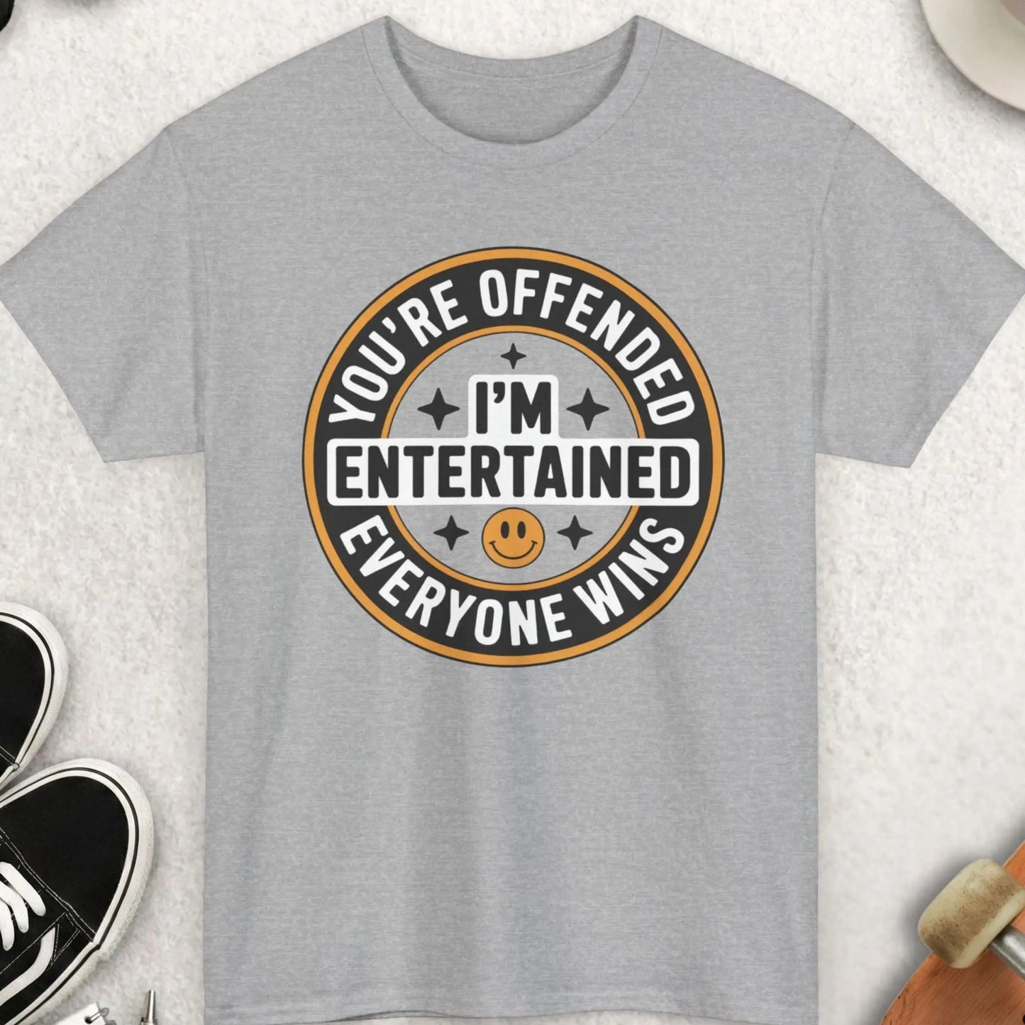 Gray t-shirt with a humorous graphic and text on a light gray surface with accessories.