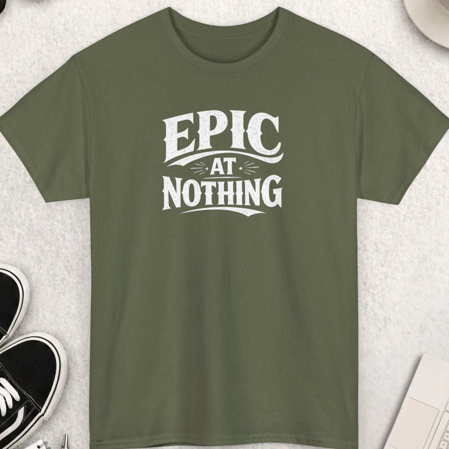 Green t-shirt with 'EPIC AT NOTHING' text on a light gray surface with accessories.