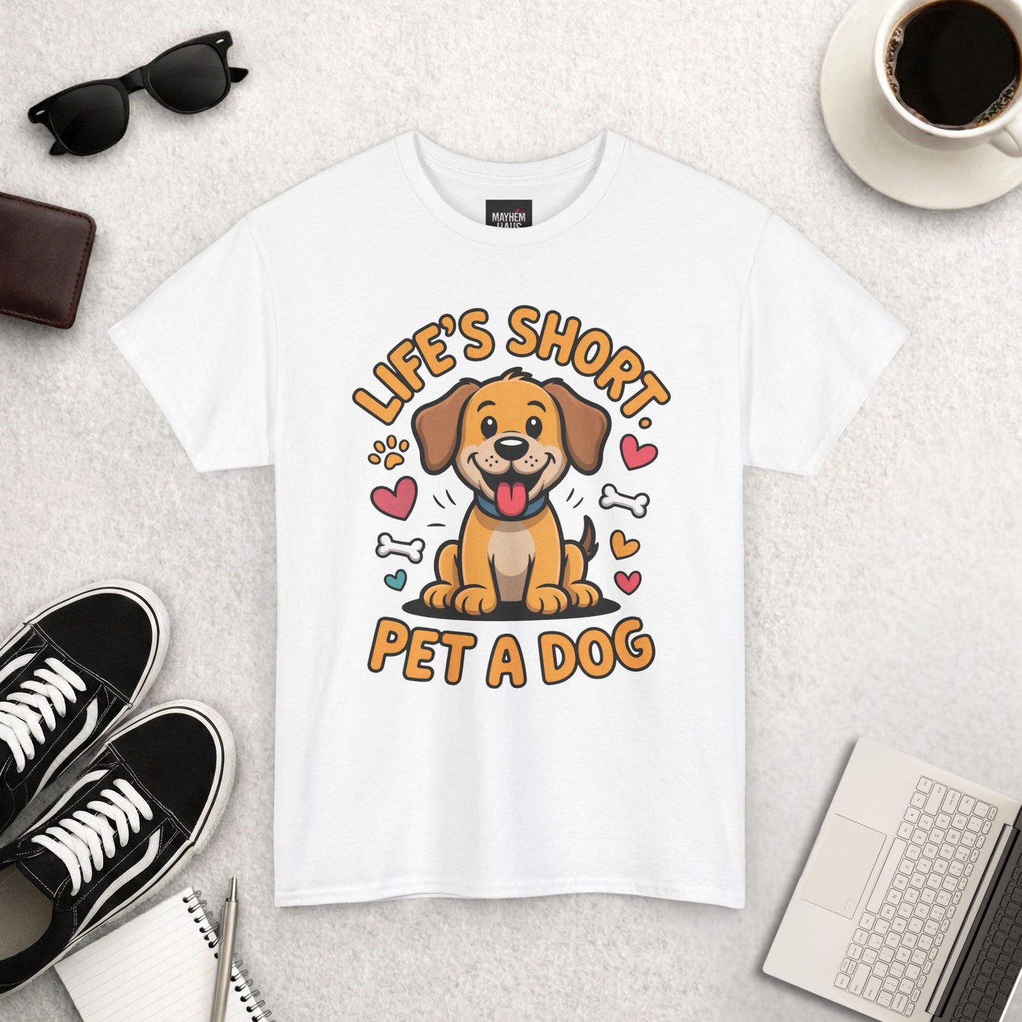 White t-shirt with a dog graphic and text 'Life's Short, Pet a Dog' on a light surface with accessories.