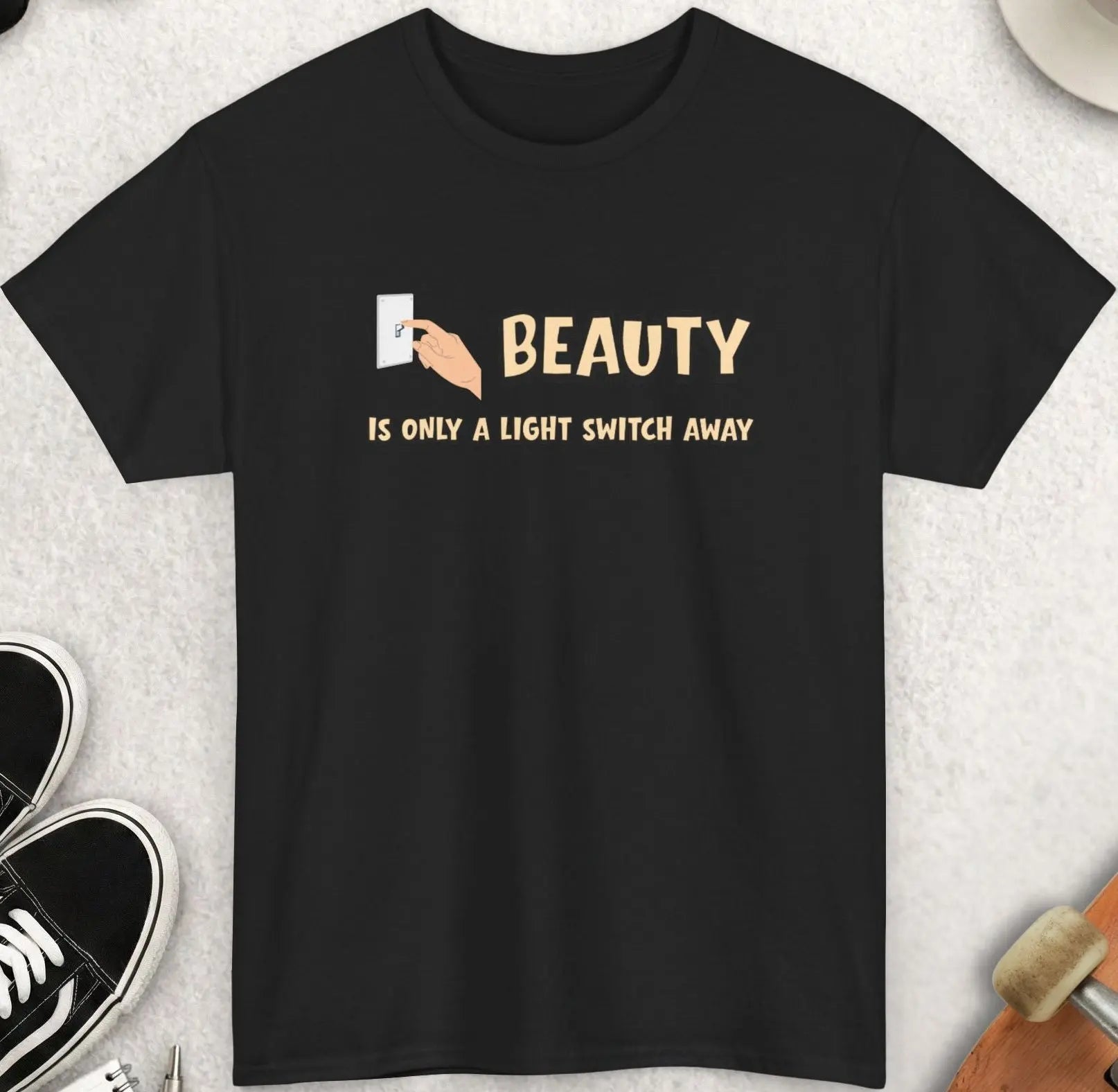 Black t-shirt with 'Beauty is only a light switch away' text on a textured surface with accessories.