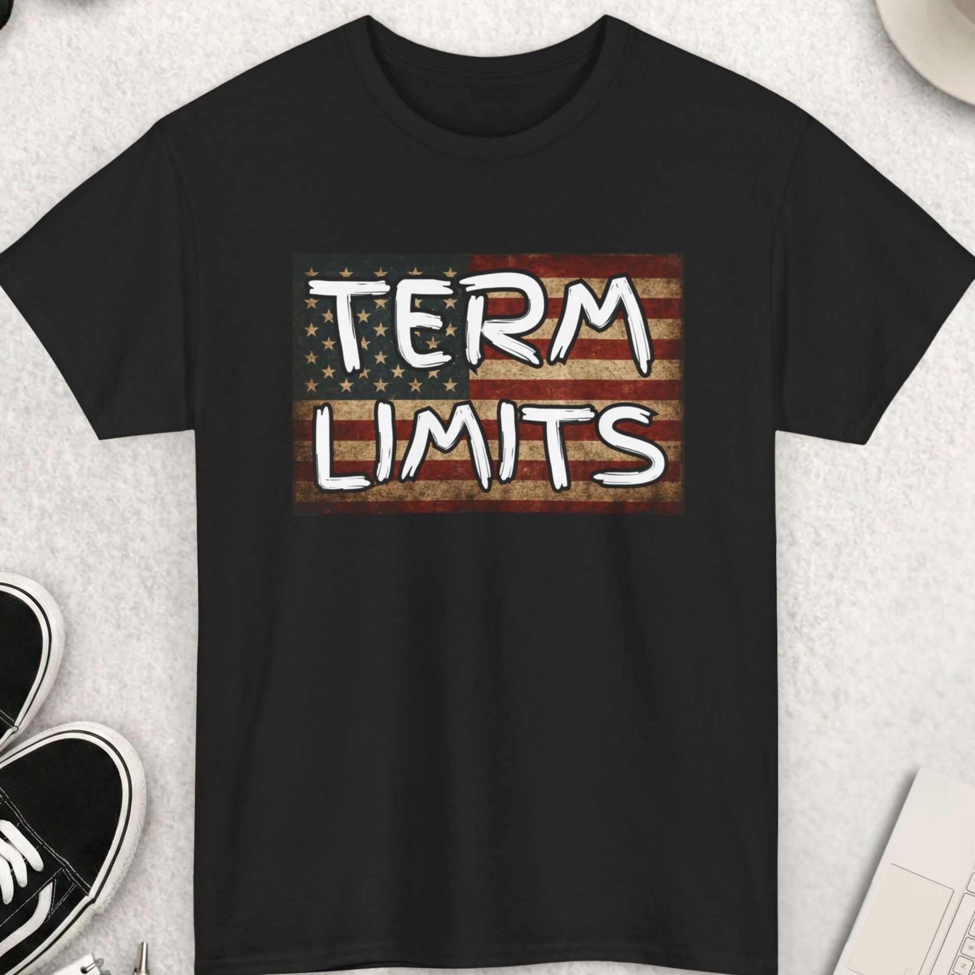 Black t-shirt with 'TERM LIMITS' text on an American flag background, placed on a light gray surface with accessories around.