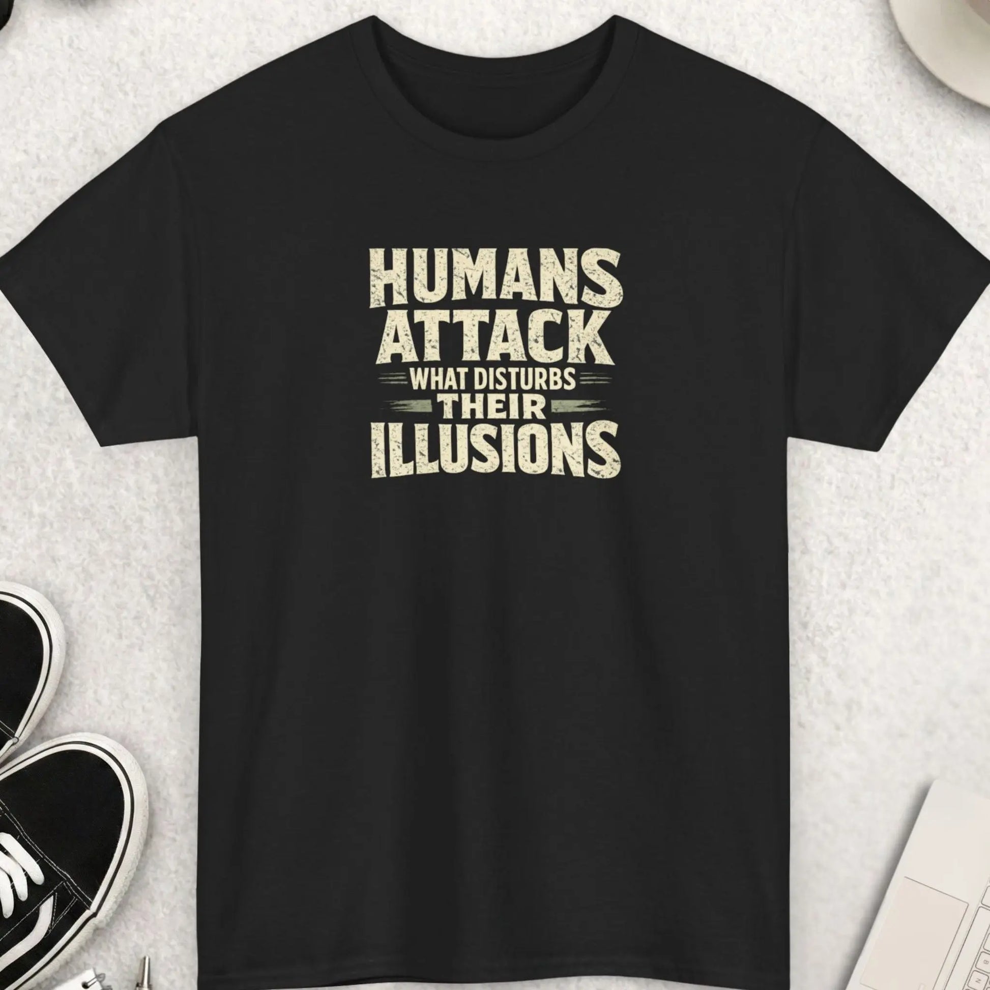 Black t-shirt featuring distressed vintage typography reading “Humans Attack What Disturbs Their Illusions” in a bold minimalist statement design.