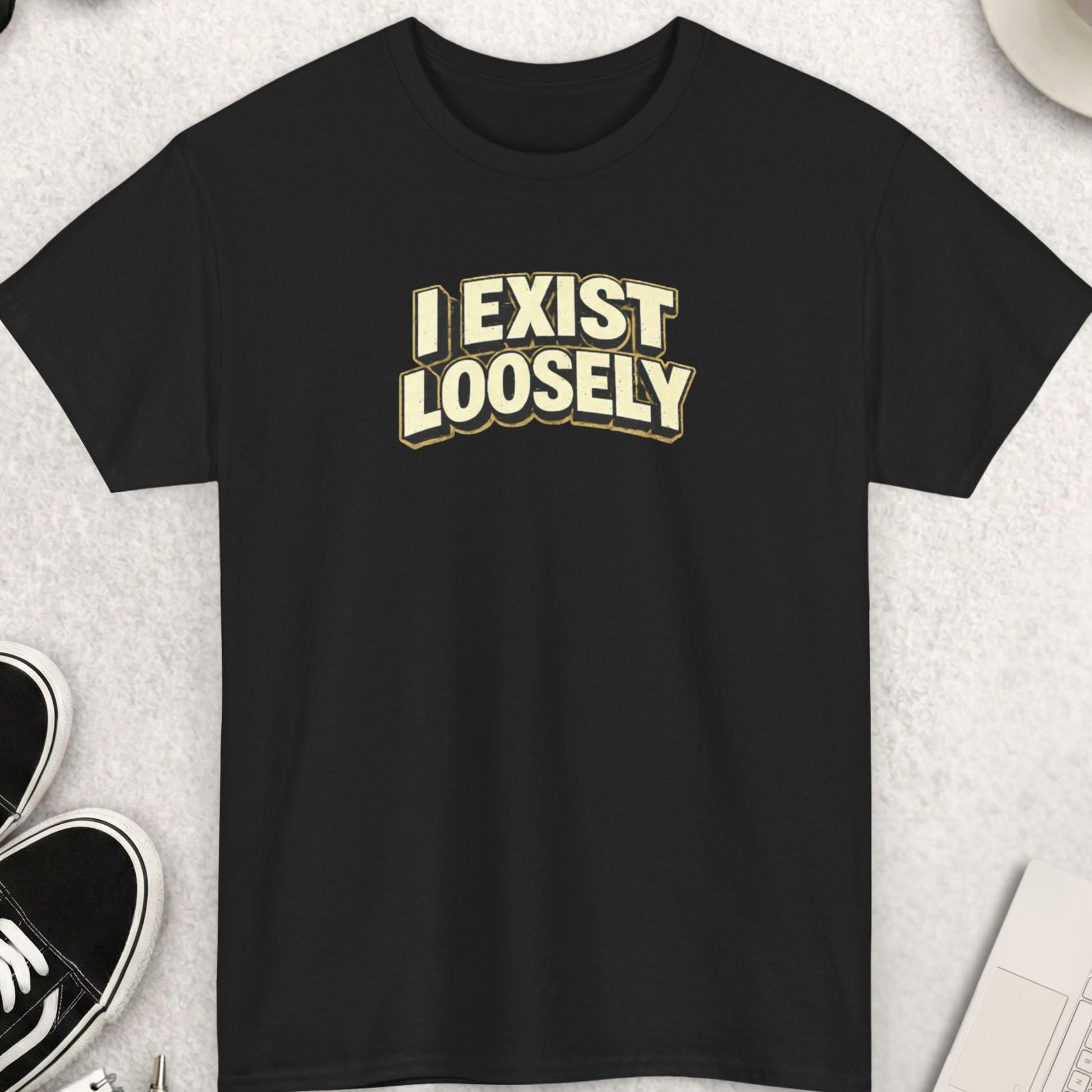 Black t-shirt with 'I EXIST LOOSELY' text on a light gray surface with shoes, coffee, and accessories.