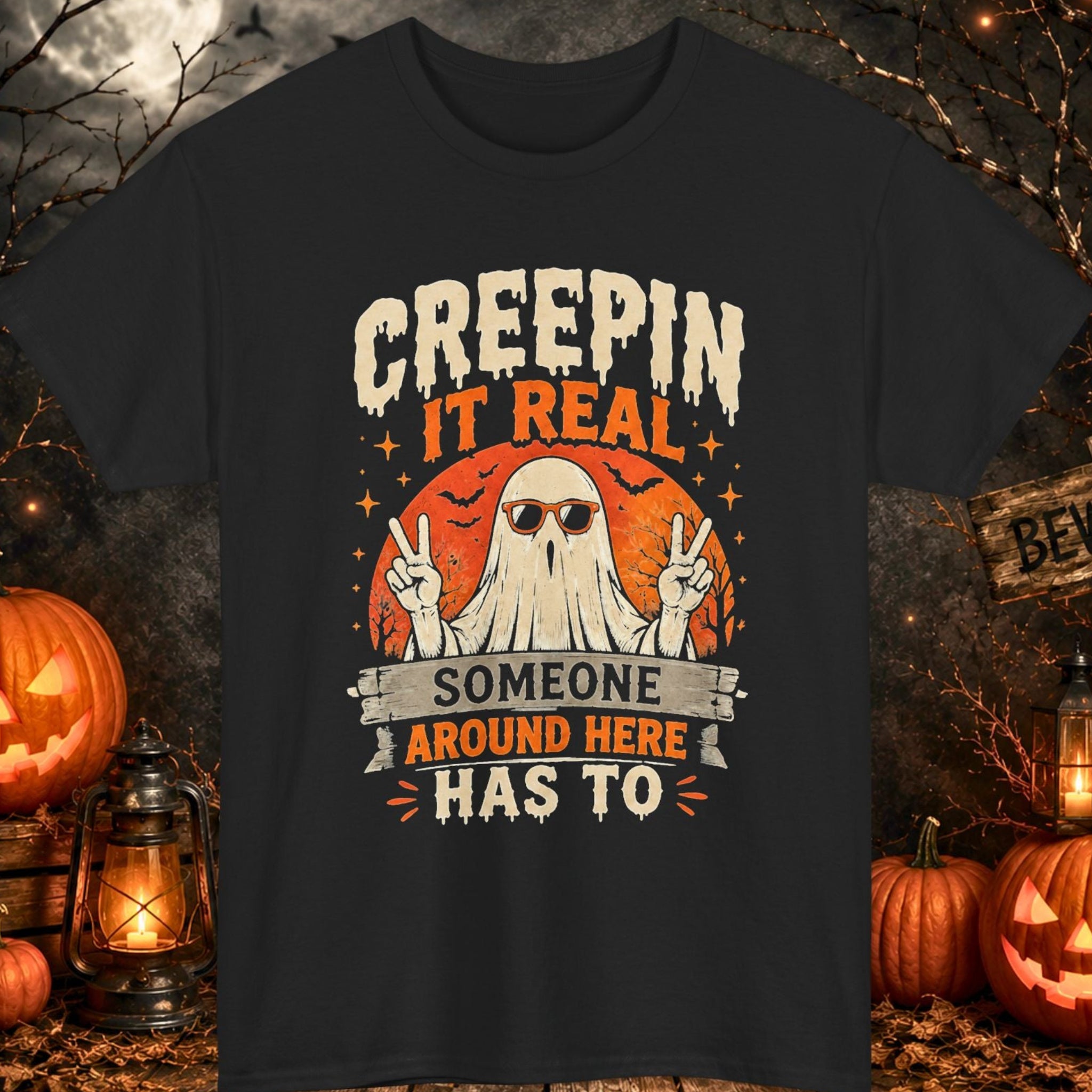 Mayhem Haus black Halloween T-shirt featuring a ghost wearing sunglasses and flashing peace signs beneath the phrase "Creepin' It Real Someone Around Here Has To." The distressed vintage design includes an orange moon backdrop, bats, and retro Halloween graphics, making it perfect for spooky season and Halloween celebrations.