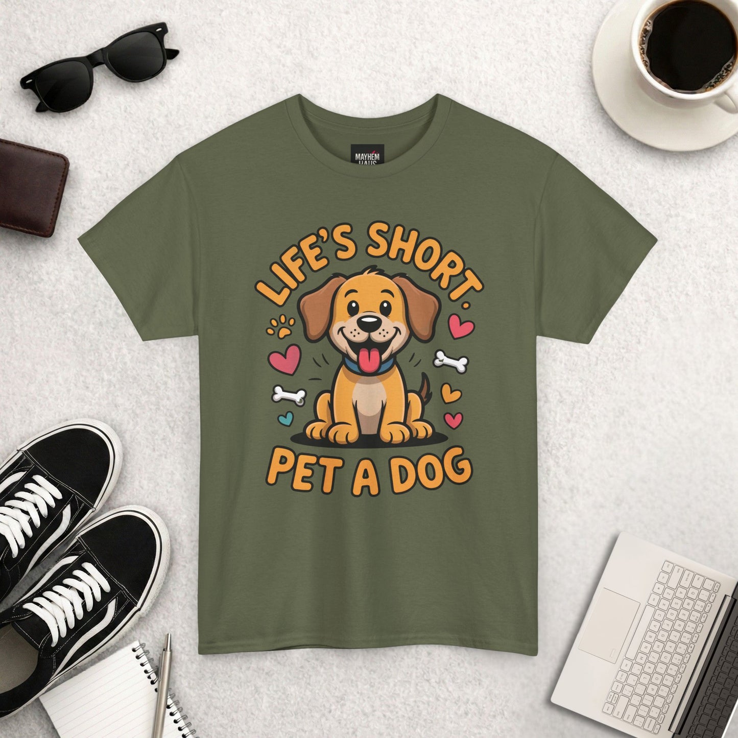 Green t-shirt with a dog graphic and text on a light gray surface with accessories.