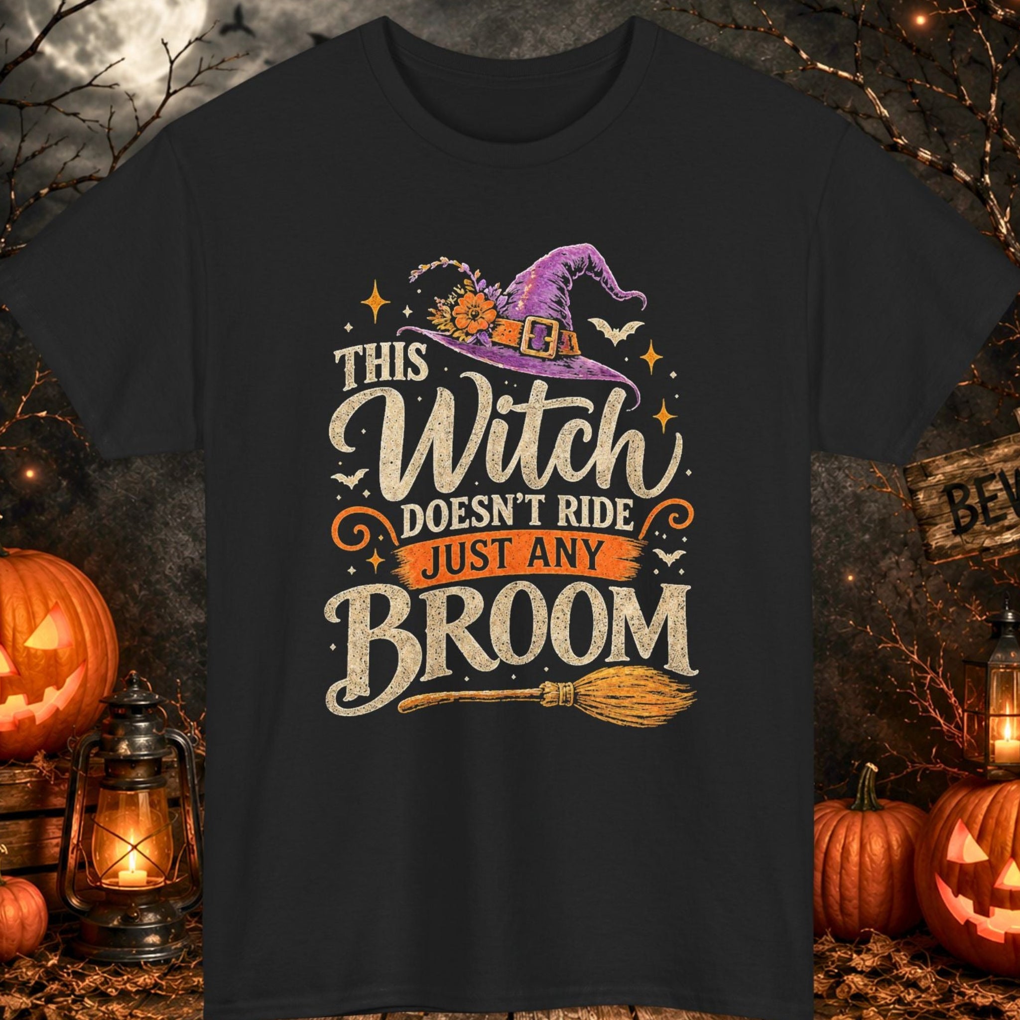 Mayhem Haus black Halloween T-shirt featuring a distressed vintage design with the phrase "This Witch Doesn't Ride Just Any Broom." The artwork includes a purple witch hat with floral accents, bats, stars, decorative typography, and a traditional broom illustrated in cream, orange, and purple.