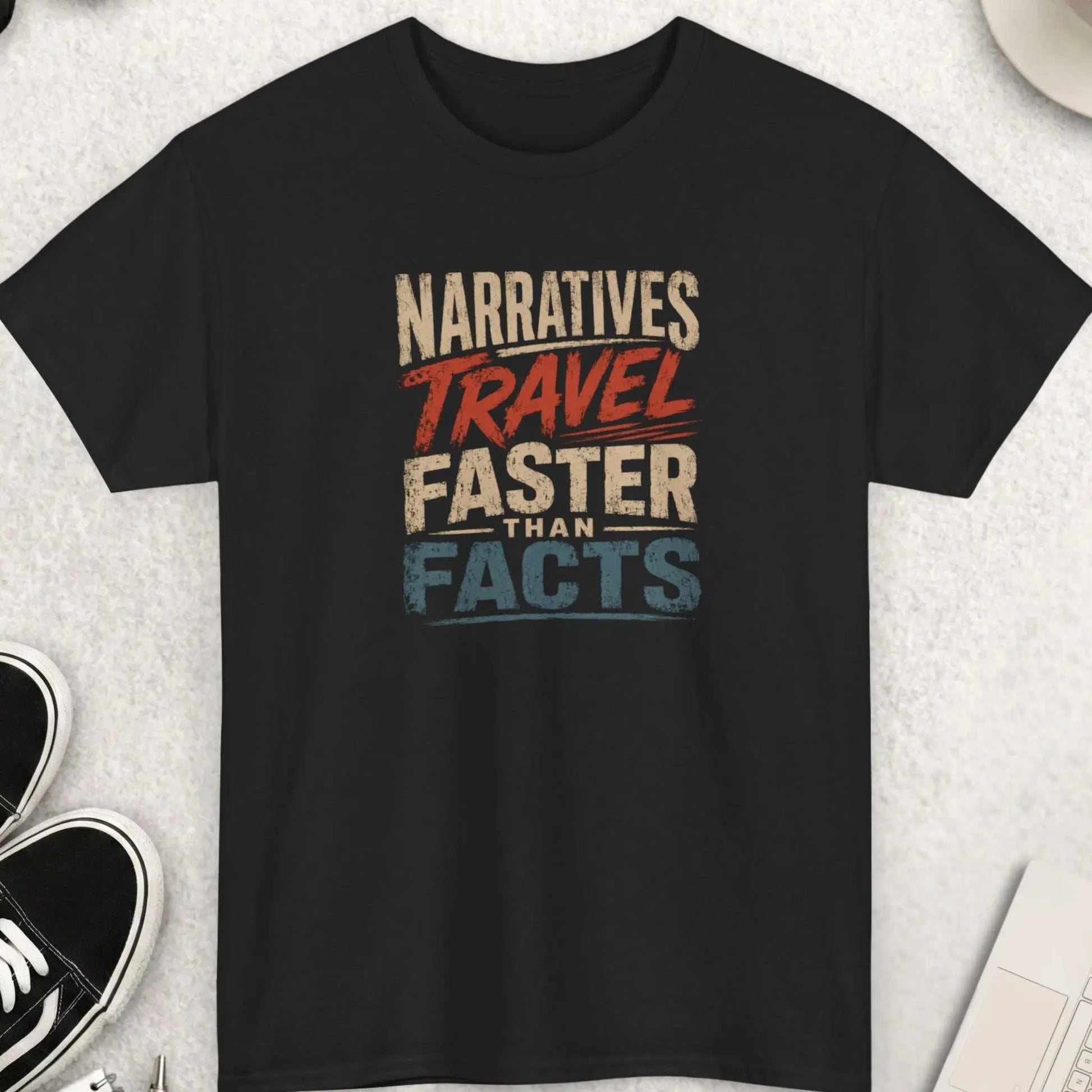 Narratives Travel Faster Than Facts distressed typography t-shirt featuring cream, rust red, and faded blue vintage lettering on a black shirt with weathered retro texture and bold statement design.