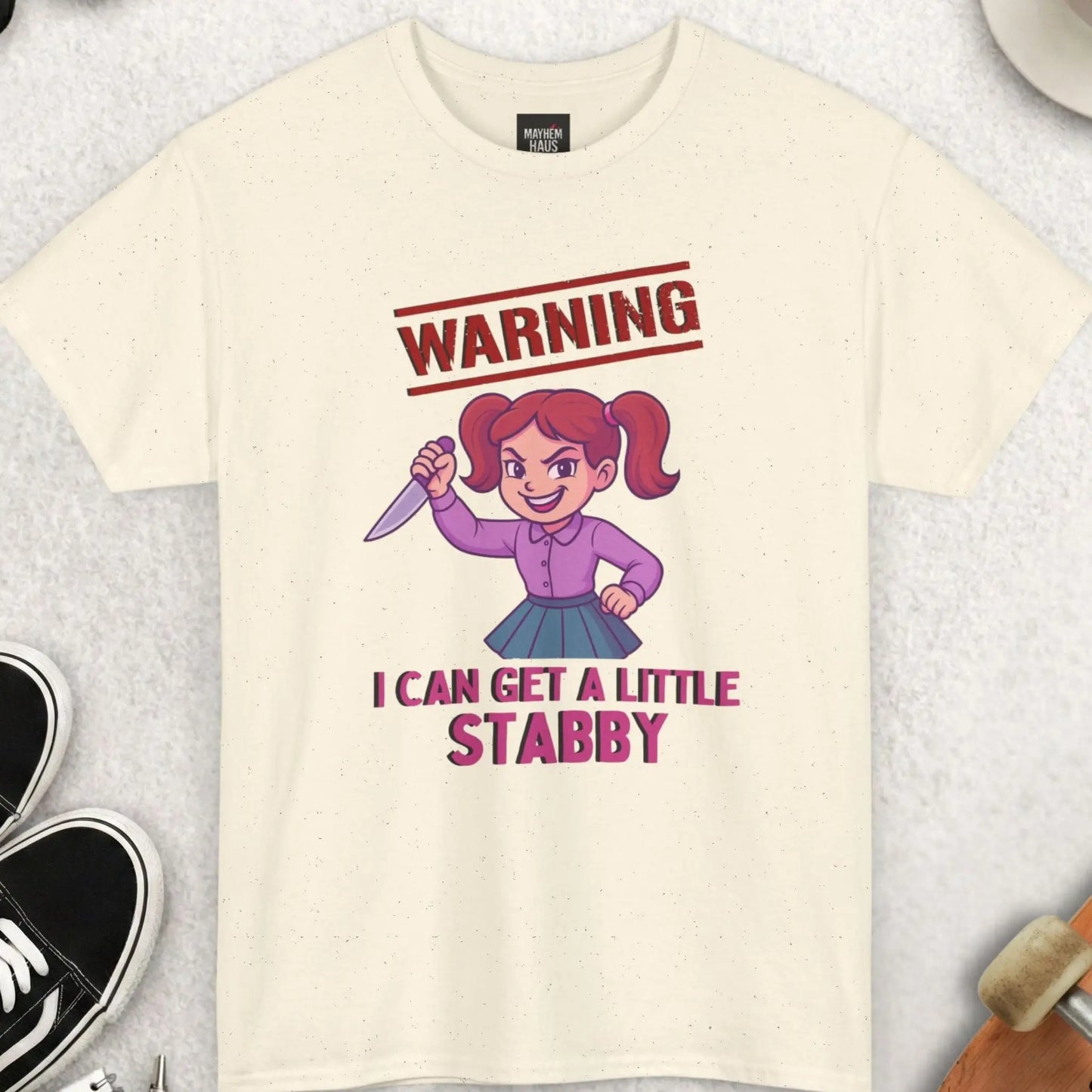 Beige t-shirt with graphic design and text on a light gray surface with accessories.